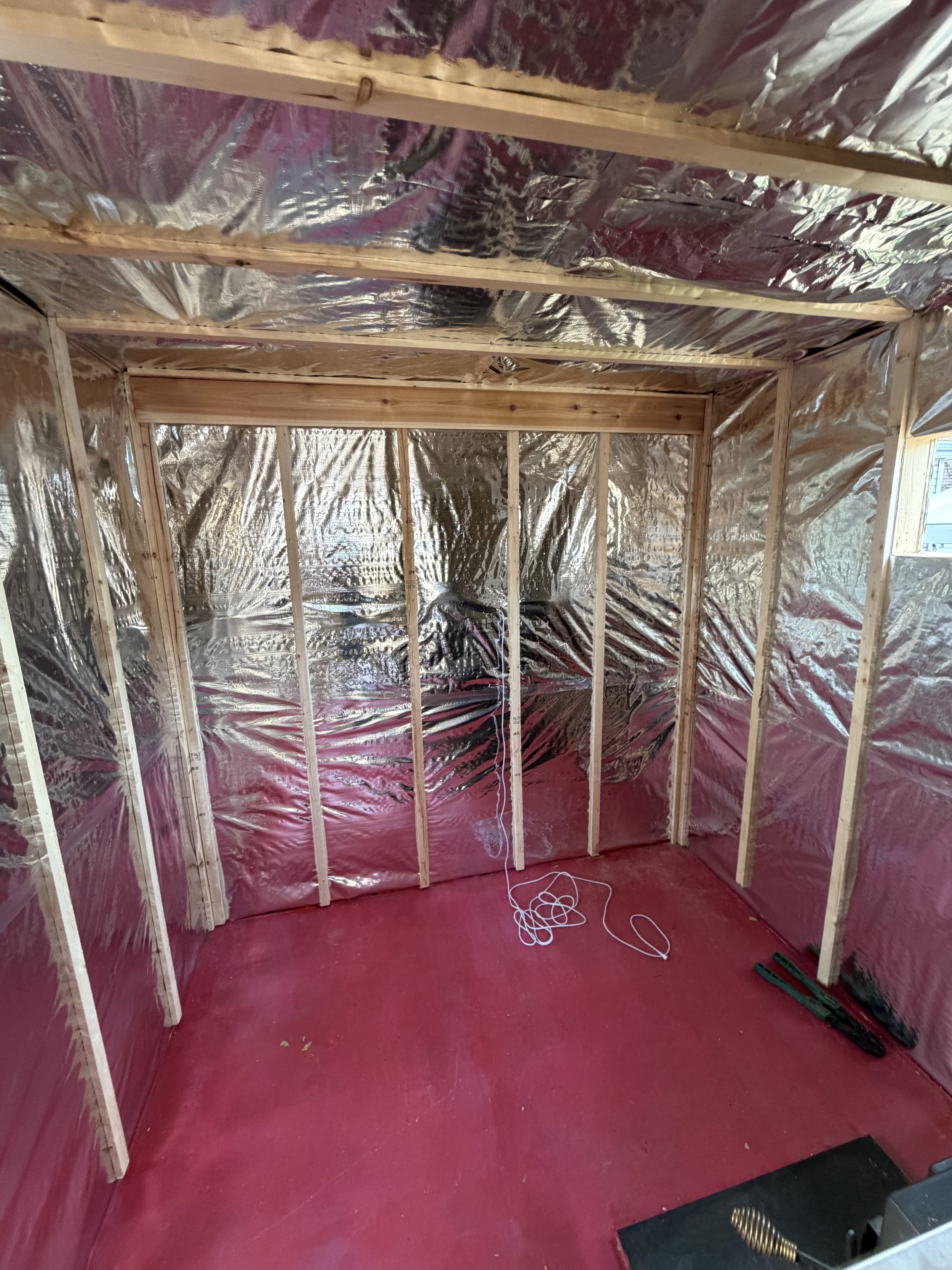 Unfinished room with pink flooring and walls lined with reflective insulation. Wooden studs are visible, indicating that the room is under construction.