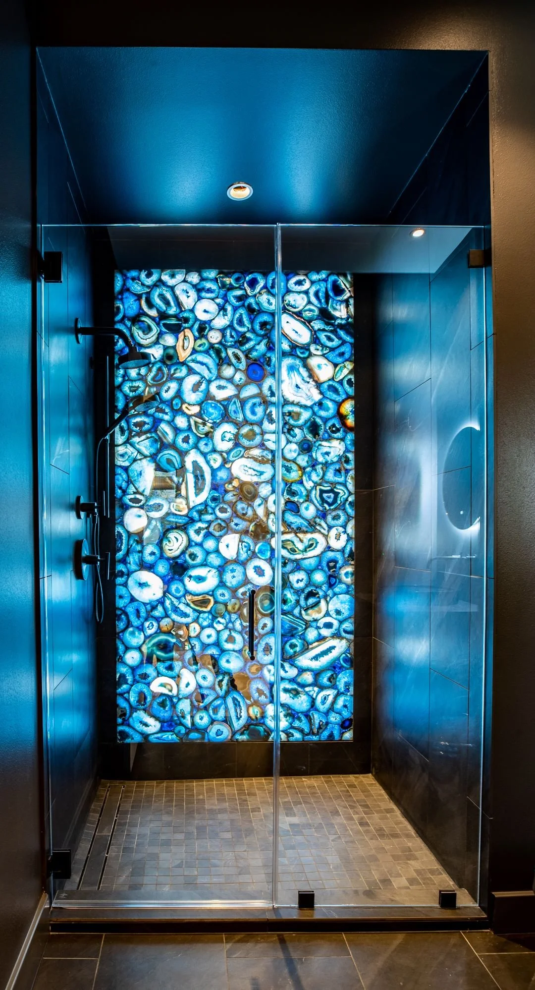 A modern shower with a colorful geode stone accent wall behind glass doors and black fixtures.