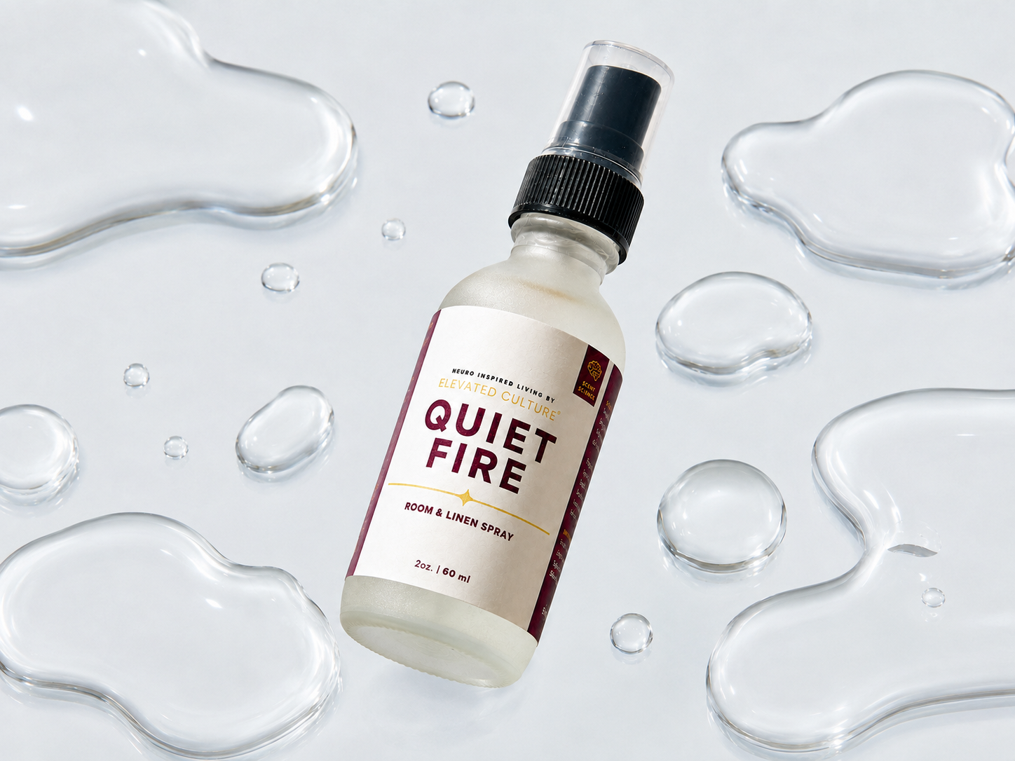 A spray bottle labeled 'Quiet Fire Room & Linen Spray' surrounded by water droplets on a light background.