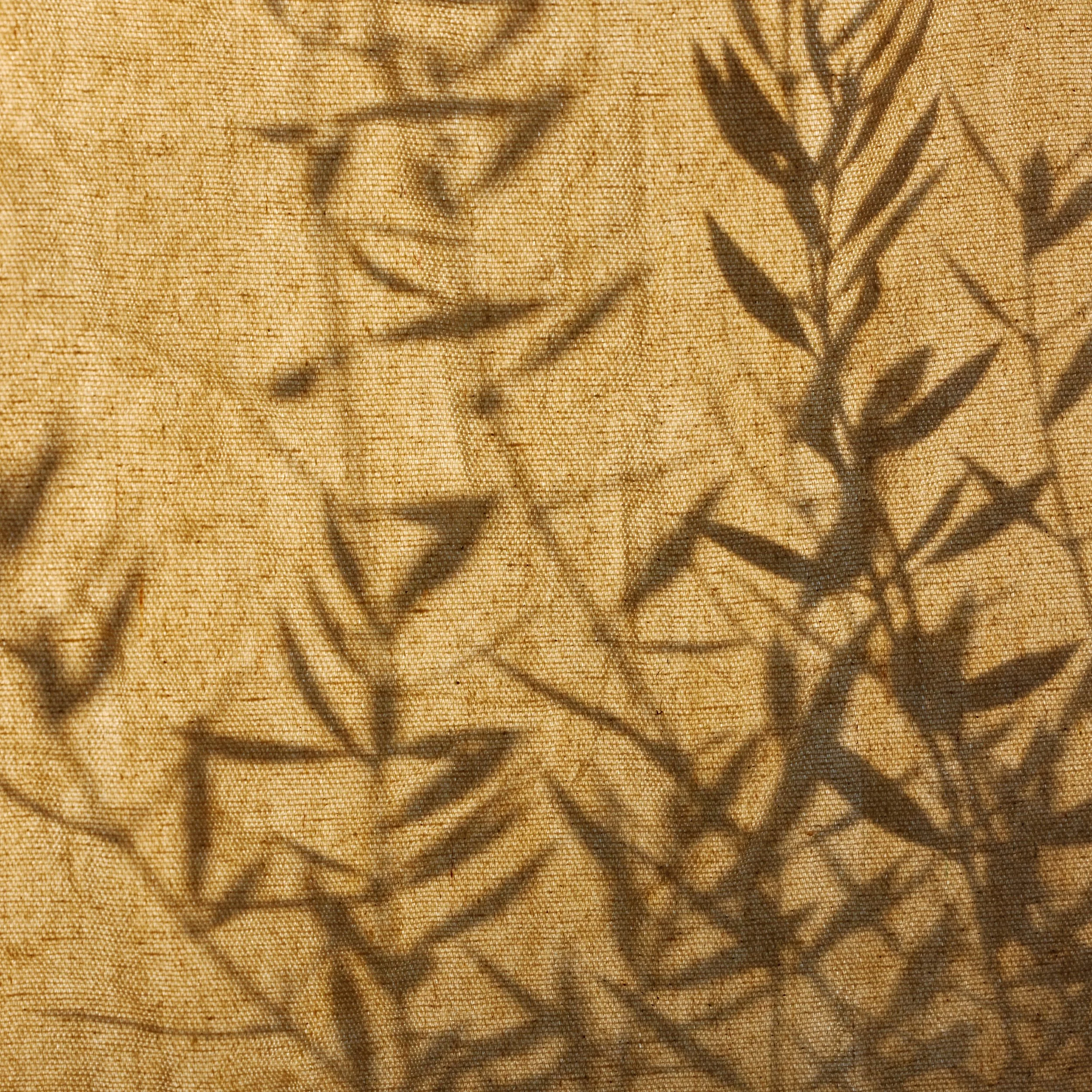 Close-up of a yellow-brown textured fabric with a faint, dark pattern.