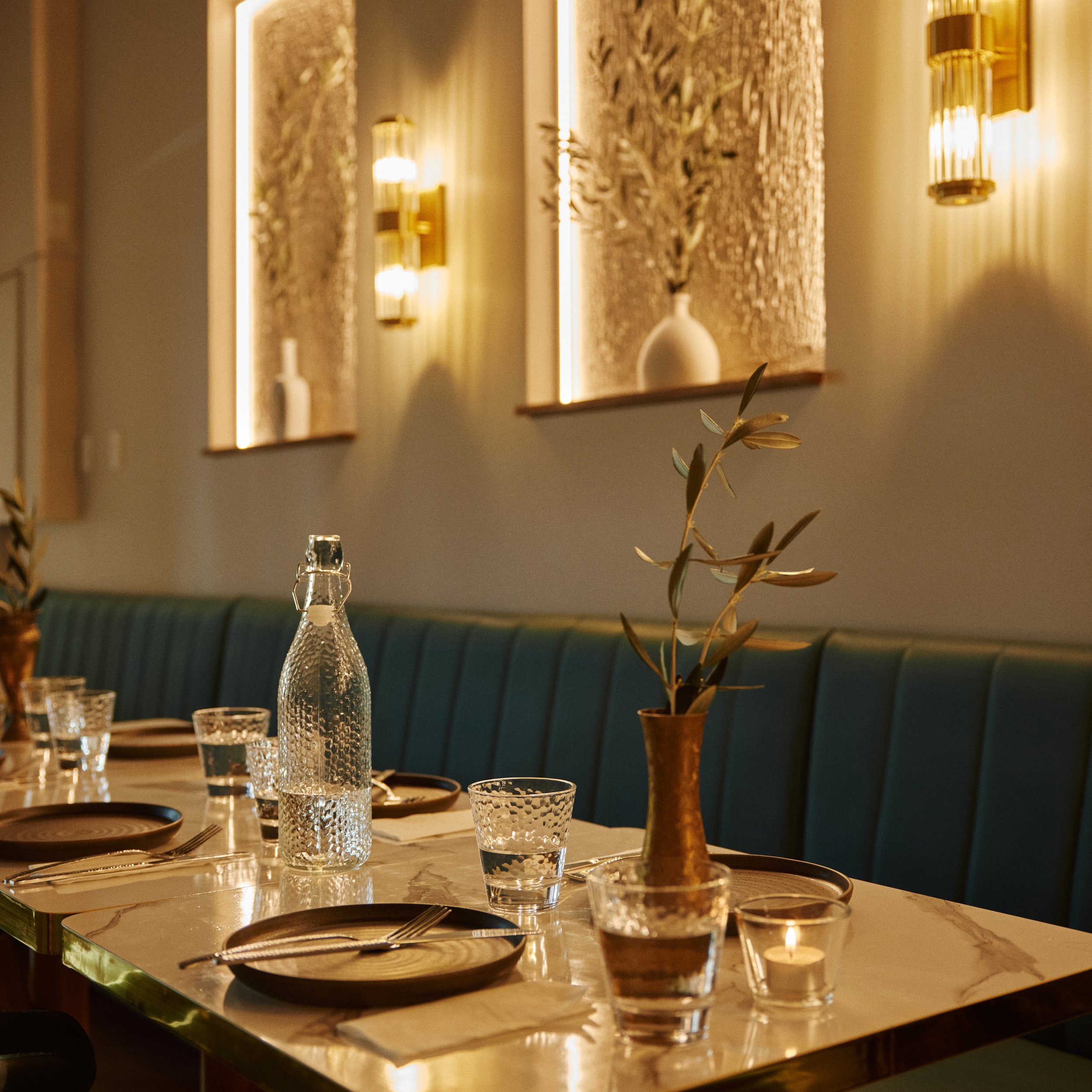 A dining table set with glassware, plates, and cutlery, with decorative vases and plants, illuminated by warm lighting in a cozy restaurant.