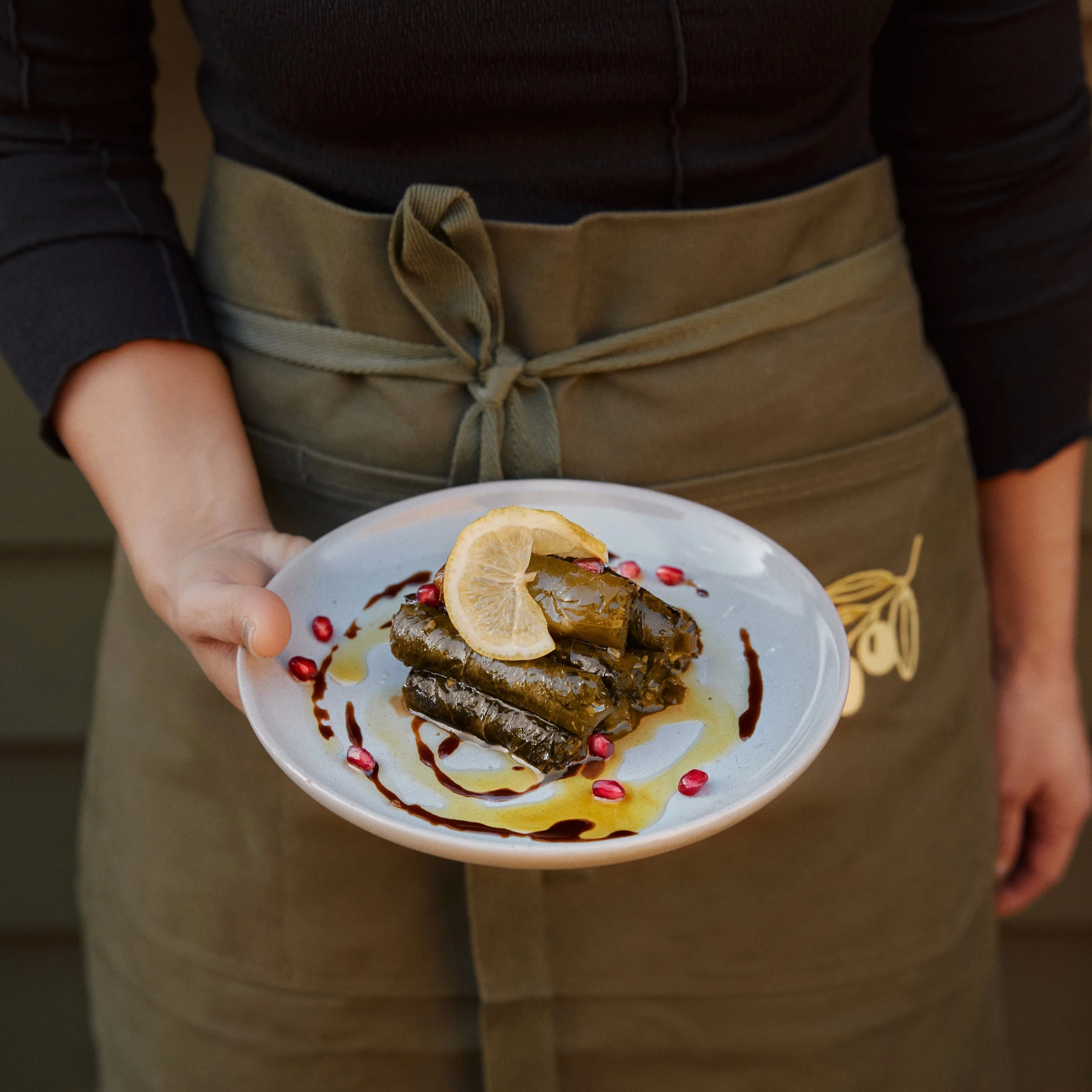 Person holding a white plate with assorted desserts, including a lemon wedge and pomegranate seeds, with a blurred background.