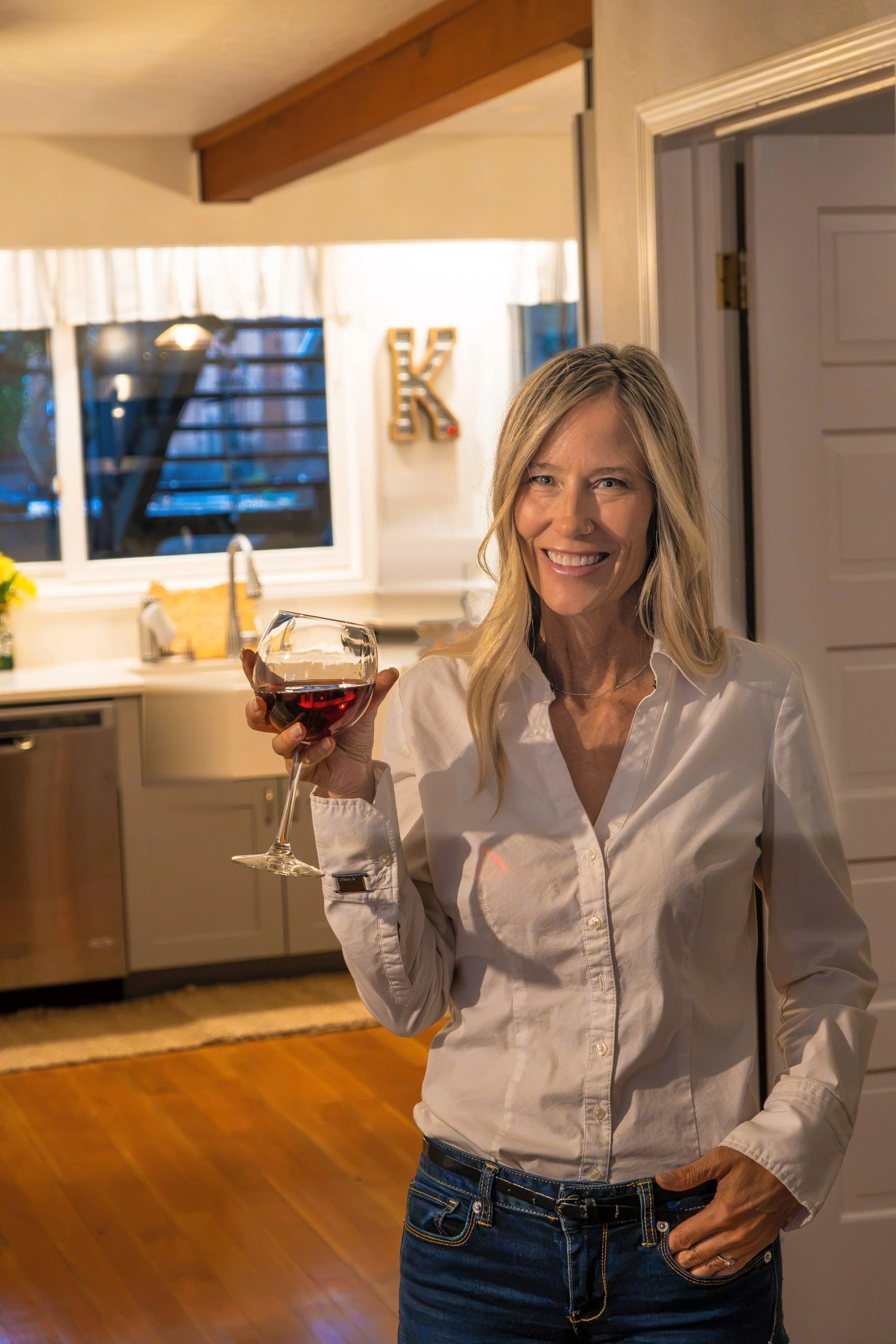 Tracy of A Curated Passport raising a glass of red wine at home.