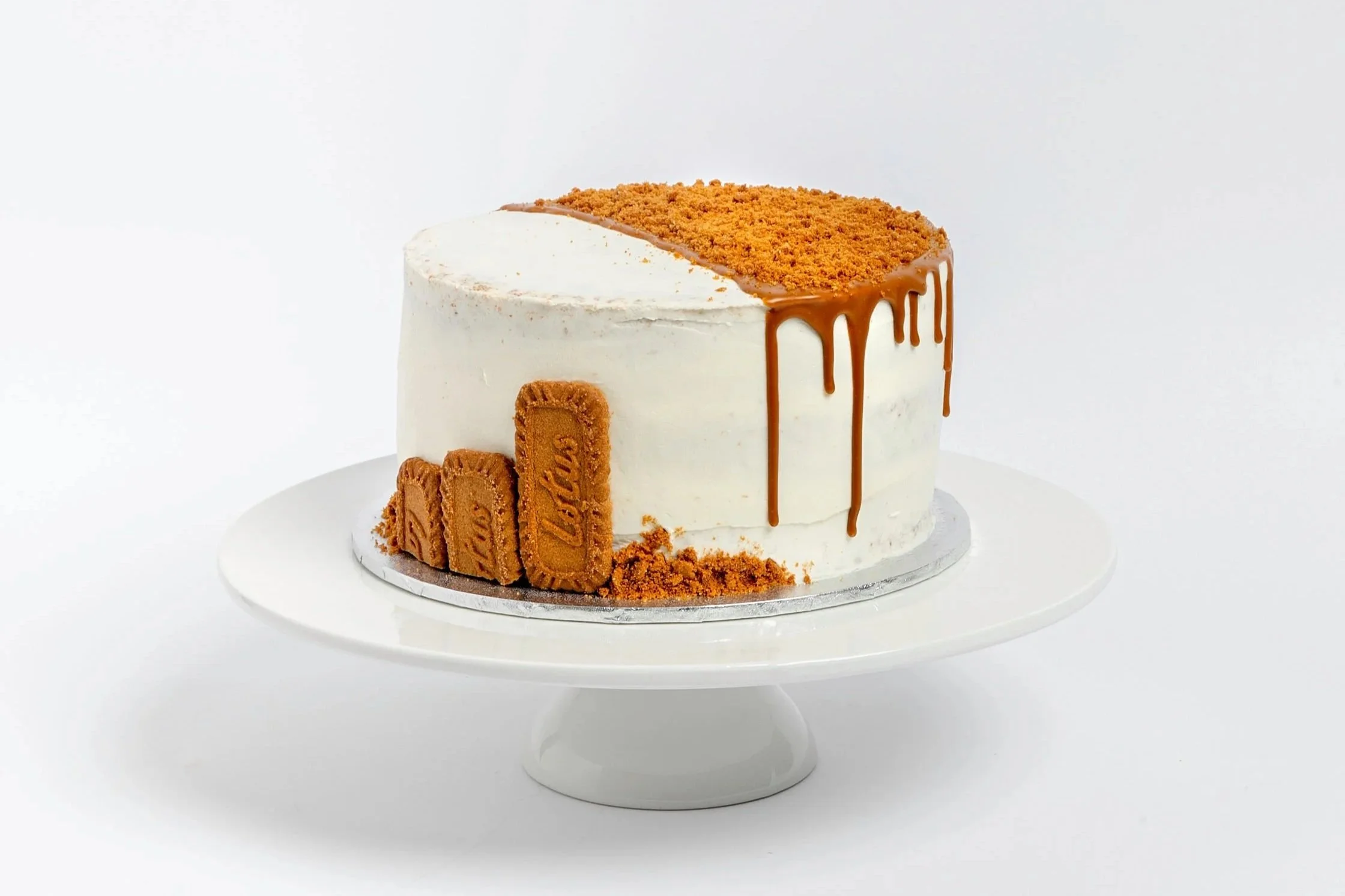 A cake decorated with biscoff biscuits, biscoff drip, and a layer of cbiscoff biscuits crumbs on top, with a white buttercream frosting exterior. Buttercream cake. biscoff cake. vegan cake. cakes in exmouth. exmouth cake