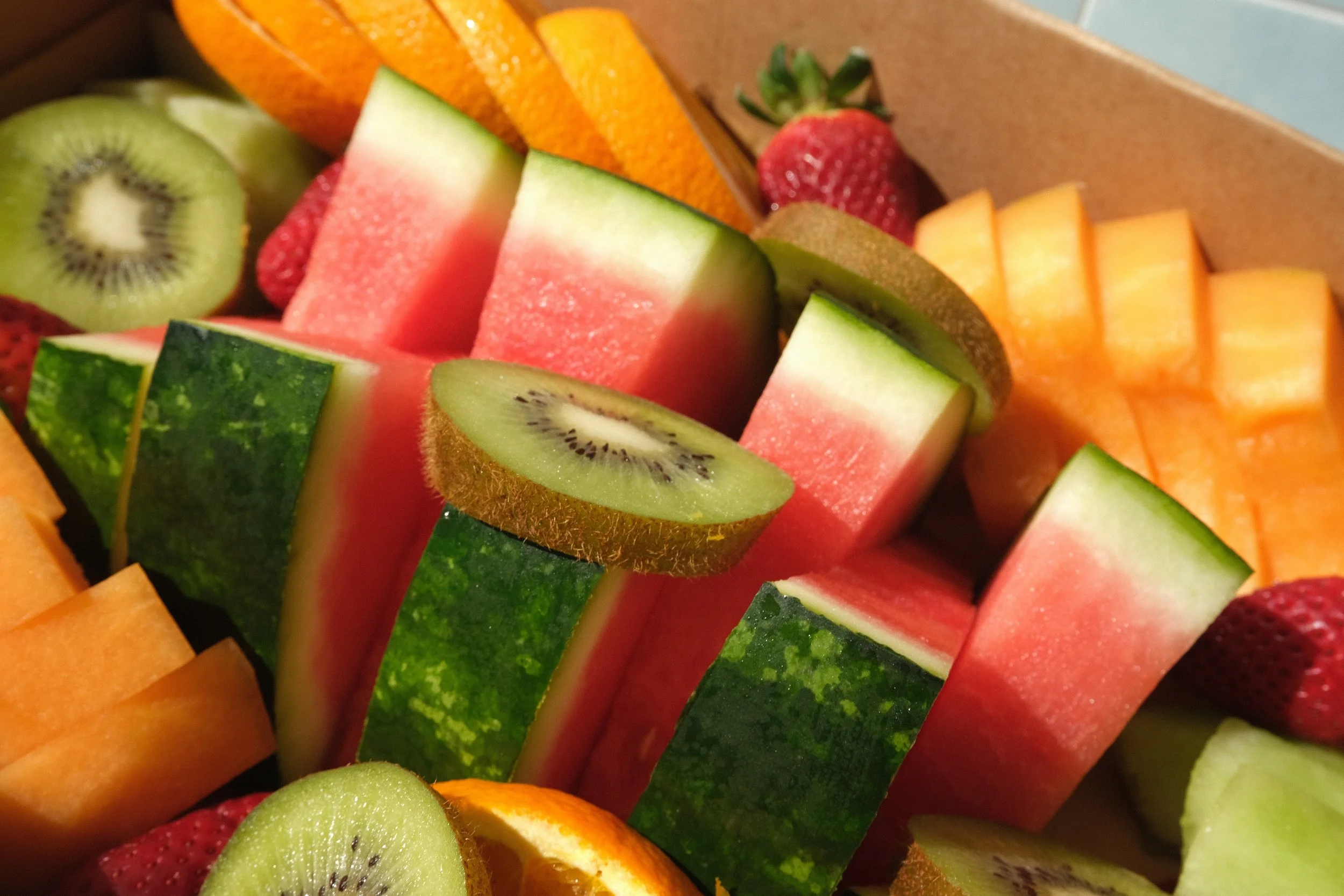 Close-up of assorted sliced fruits including kiwi, watermelon, cantaloupe, strawberries, honeydew, and orange. catering. fruit platter. catering boxes exmouth