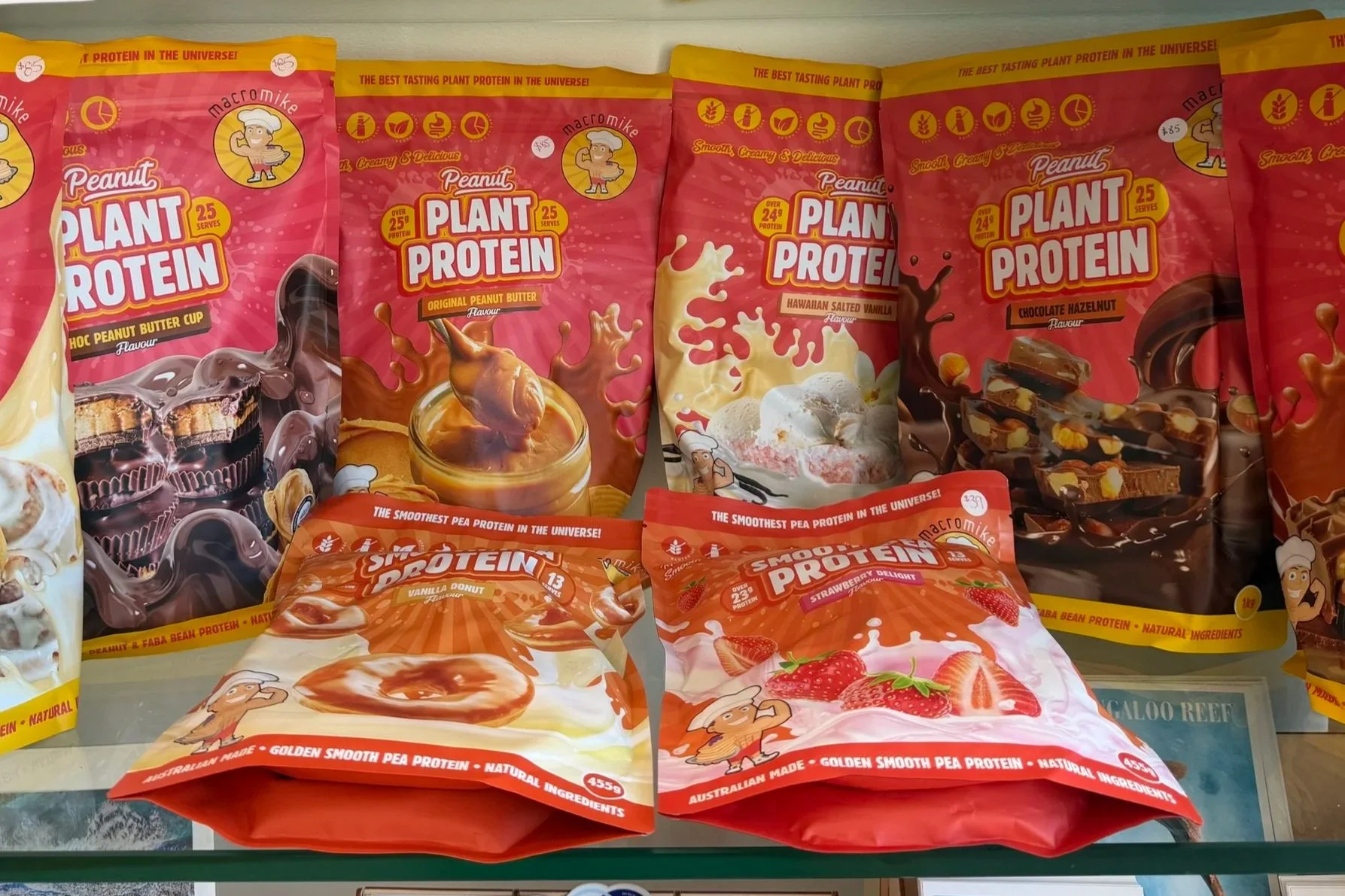 Assorted plant-based protein snack packs with colorful packaging, featuring various flavors such as peanut butter, vanilla donut, strawberry delight, and chocolate hazelnut, displayed on a store shelf. Macro Mike Protein
