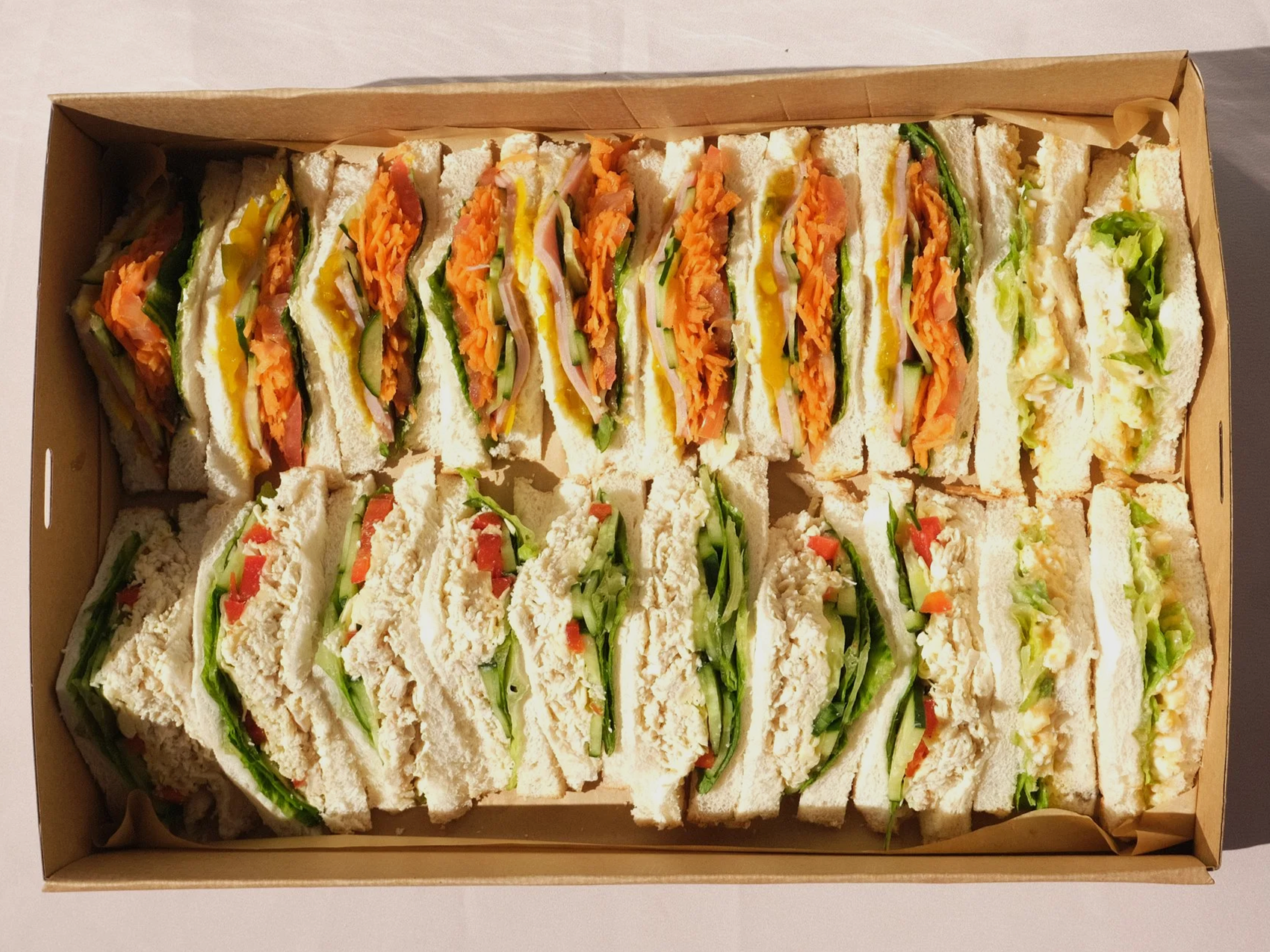 A box of various club sandwiches with layers of bread, lettuce, tomato, cheese, and deli meats.  catering. sandwich platter. catering boxes exmouth