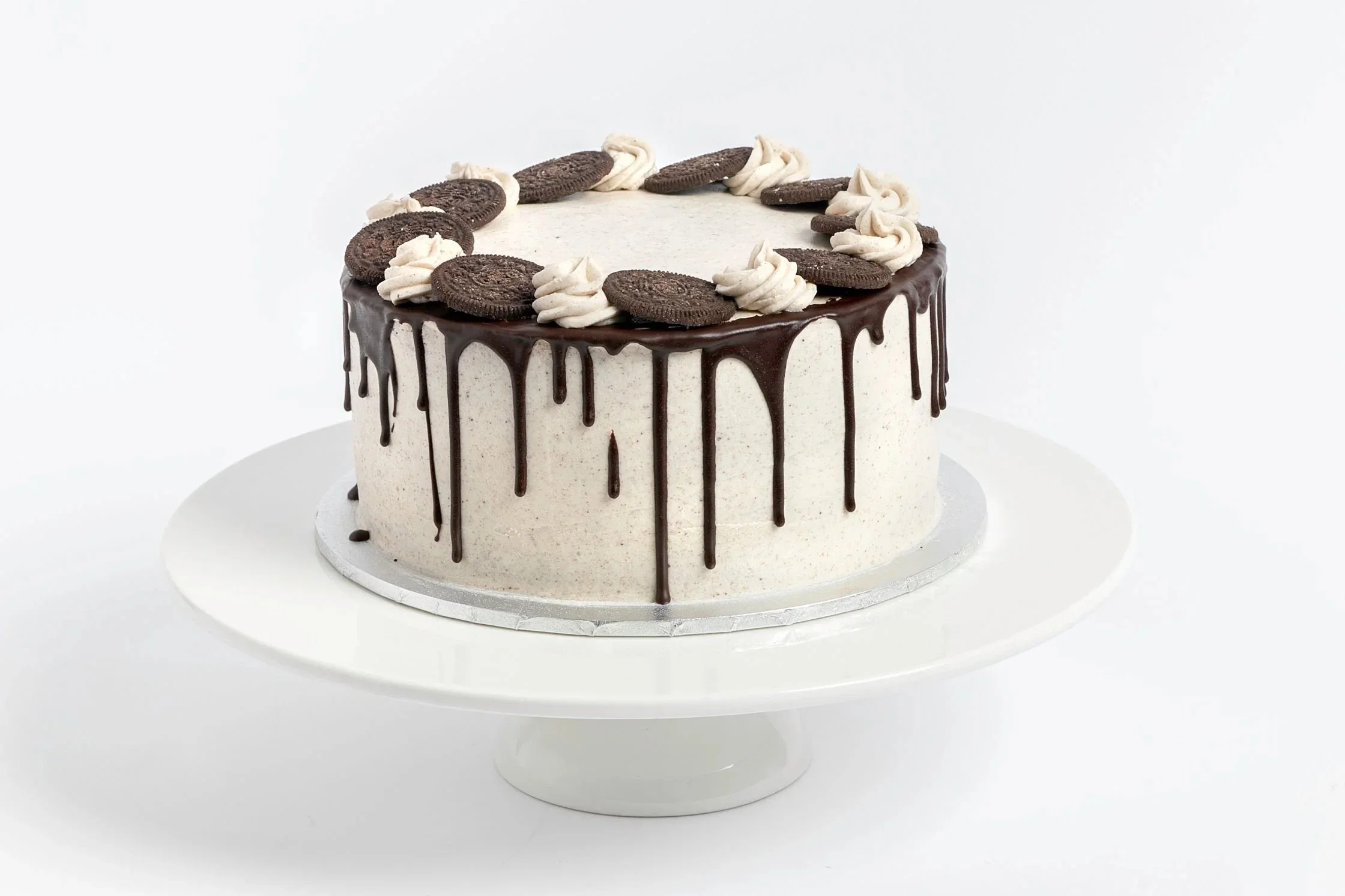 A round cake decorated with Oreo cookies on top and chocolate glaze dripping down the sides, placed on a white cake stand. Buttercream cake. oreo cake. cake. vegan cake. cakes in exmouth. exmouth cake