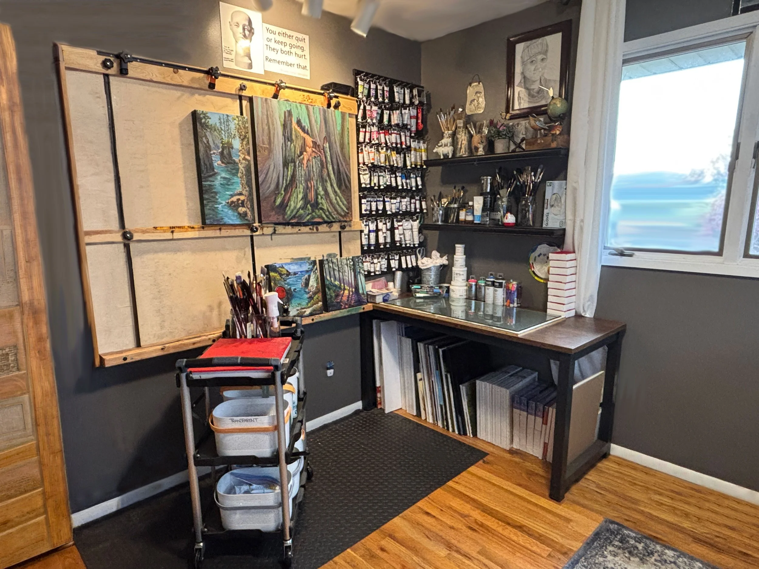 Home art studio with landscape paintings, paintbrushes, tubes of paint, and art supplies.
