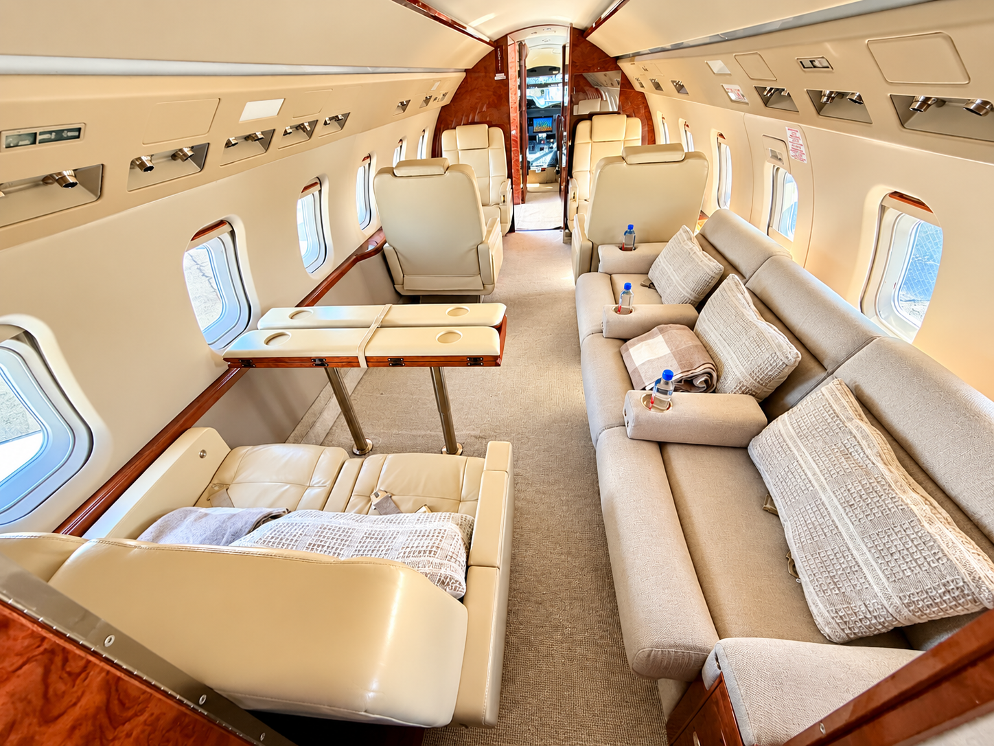 Luxury Challenger 604 private jet cabin interior featuring cream leather seating, spacious sofa, polished wood accents, and elegant furnishings at McClellan-Palomar Airport in Carlsbad, California.