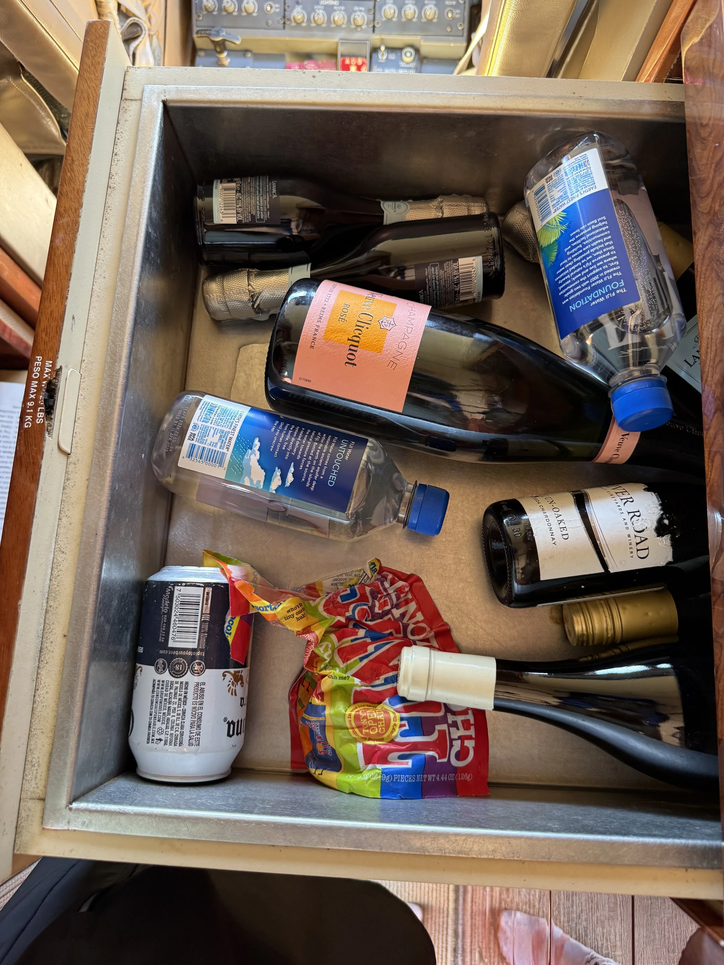 Before cleaning: Aircraft galley storage compartment aboard a Challenger 604 private jet, containing beverage bottles, melted ice water, and miscellaneous items prior to interior detailing by San Diego Aircraft Detailers.