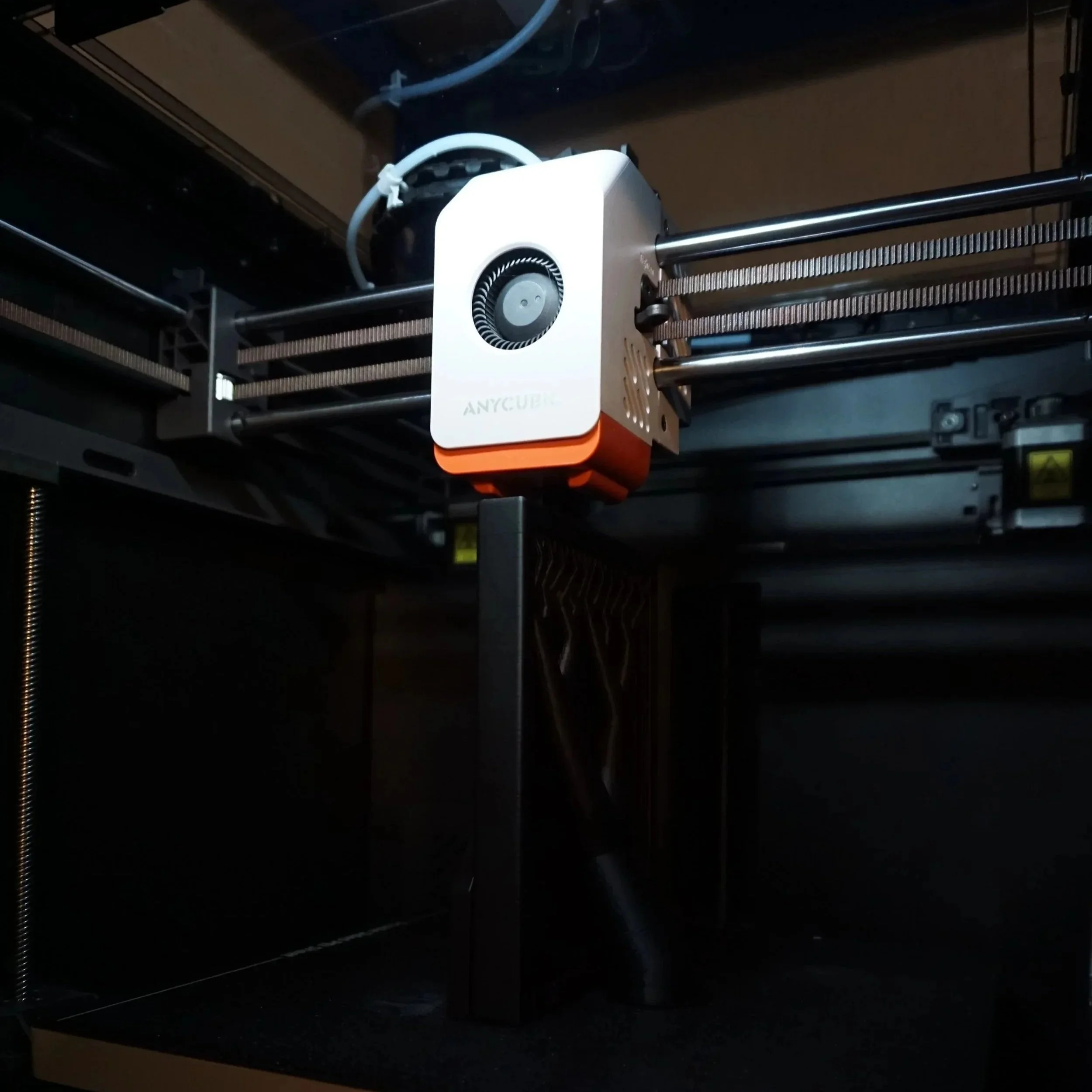 An Anycubic 3D printer moving its extruder along a metal rail, with a dark area around the printer.