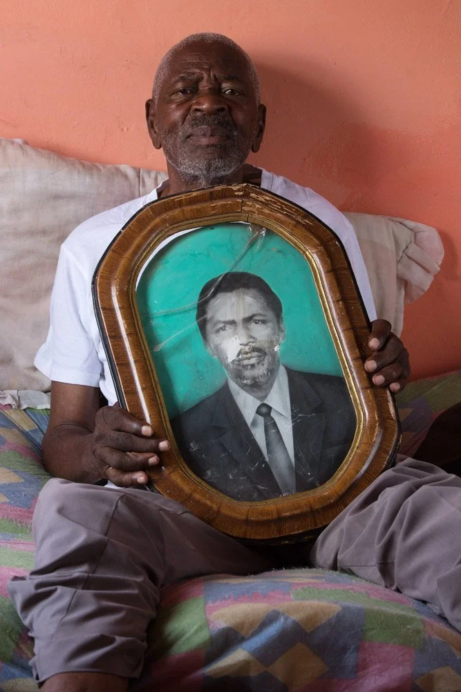 Gideon Sefuba, son of Moses Sefuba and Tebora Thwalo, holds a portrait of his father. Father Moses worked as a shop assistant for a certain Jeffreys, who ran the village general store. After 30 years he opened his own shop. Uncle Gideon bred and sold