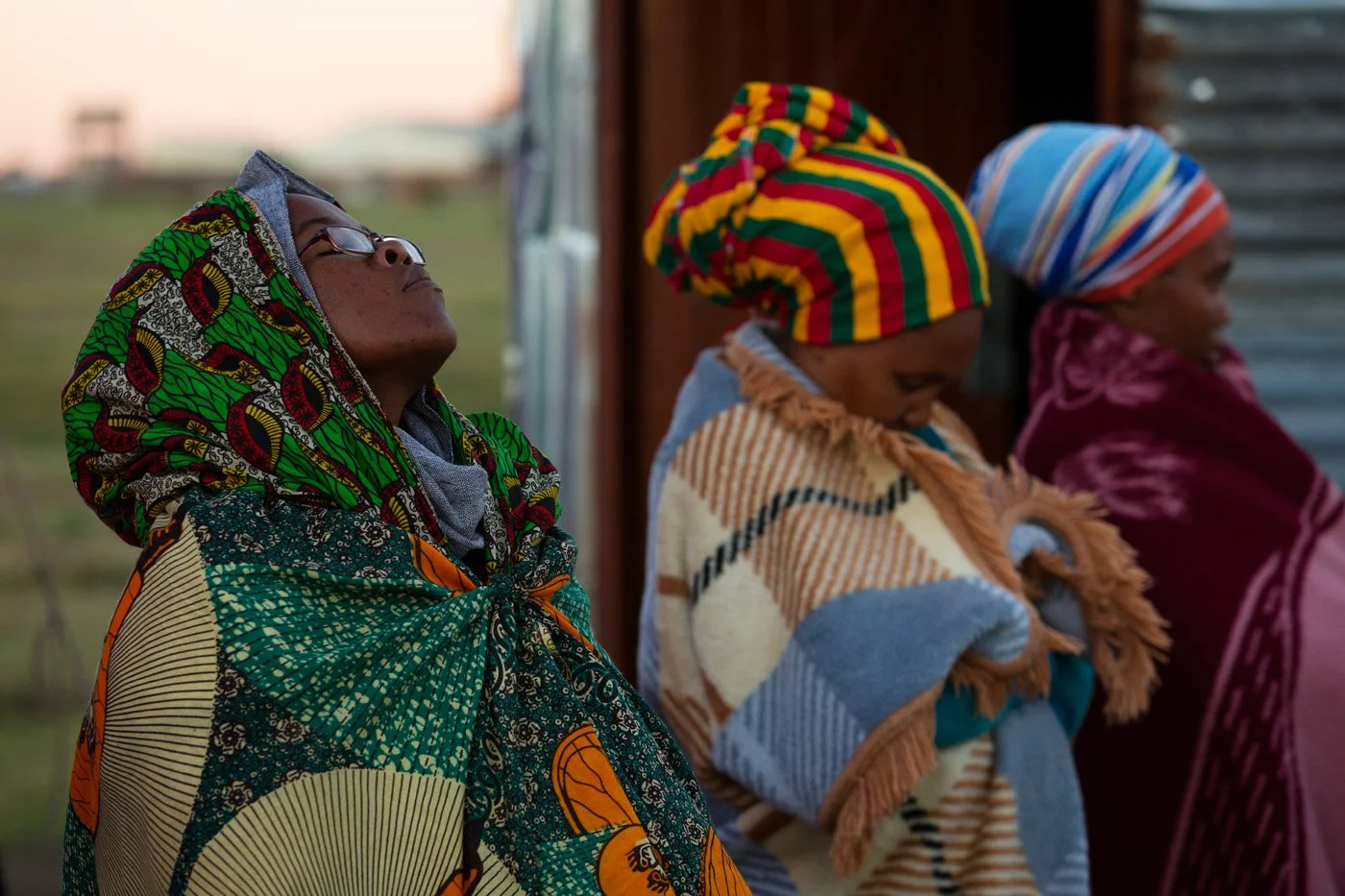 Wrapped in blankets to keep the cold at bay, three sistren are lost in thought.
