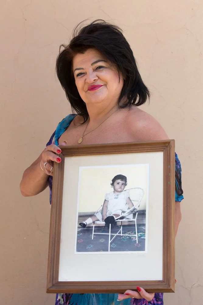 Friedel Smith holds a framed, hand-coloured analog black-and-white print of a portrait depicting herself as a one-year-old. Friedel was put up for adoption right after birth. Her mother, who was 19 when the baby was born, would have been frowned upon