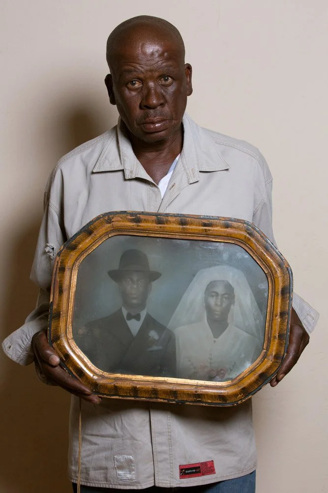 Janie John Tladi holds the framed, hand-coloured wedding portrait of his parents, Jacob Rajani Tladi and Mathapelo Miriam Tladi. The couple married in 1950. Janie's father worked at the post office but he also owned cattle and sold milk. His mother w