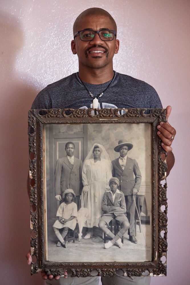 Khotso Pudumo holds a framed analog black-and-white print of the wedding portrait of his maternal great-grandparents, Samuel Tlale Nkone and Rosta Nobelungu Nkone. Great-grandfather Samuel was a prison warden, Gran Rosta a domestic worker.  Mr. Pudum