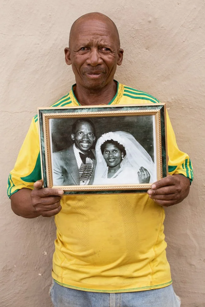 Majoro Elias Potsanyane and his late wife Gladys. Majoro holds a a framed black-and-white photograph, a cherished souvenir of their wedding day on the 30th of November 1977. Gladys passed away a few days short of the couple's 32nd wedding anniversary