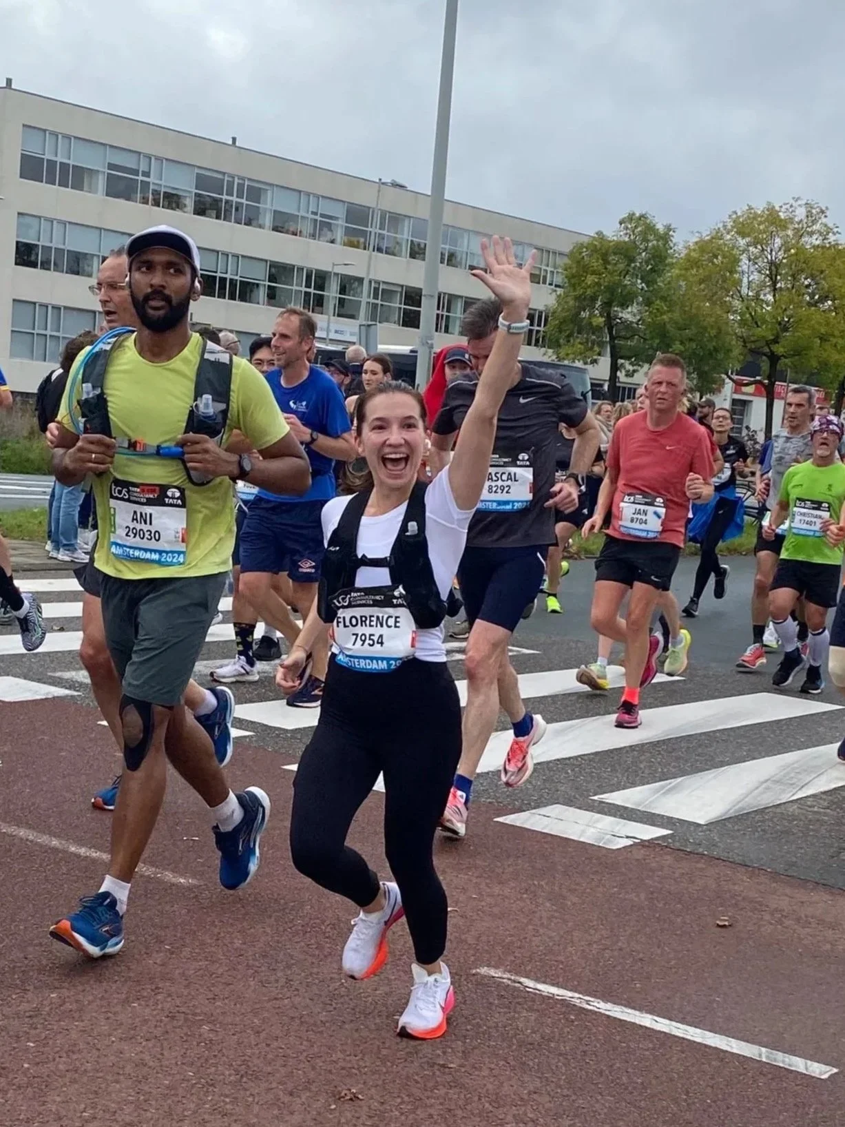 A group of marathon runners participating in a race in an urban area, with some smiling and waving at the camera.
