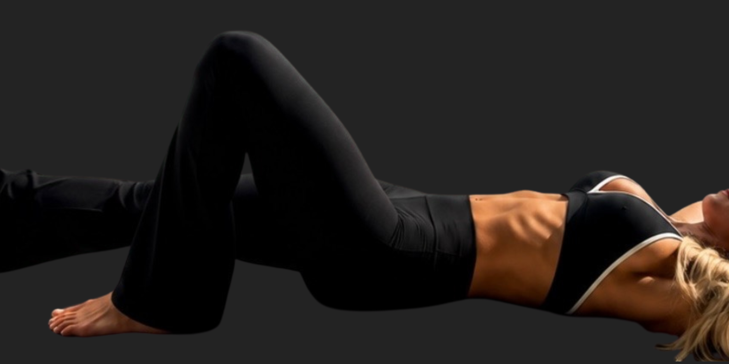 A woman lying on her side wearing black workout clothes and protective sports gear, with her head turned to the side against a dark background.