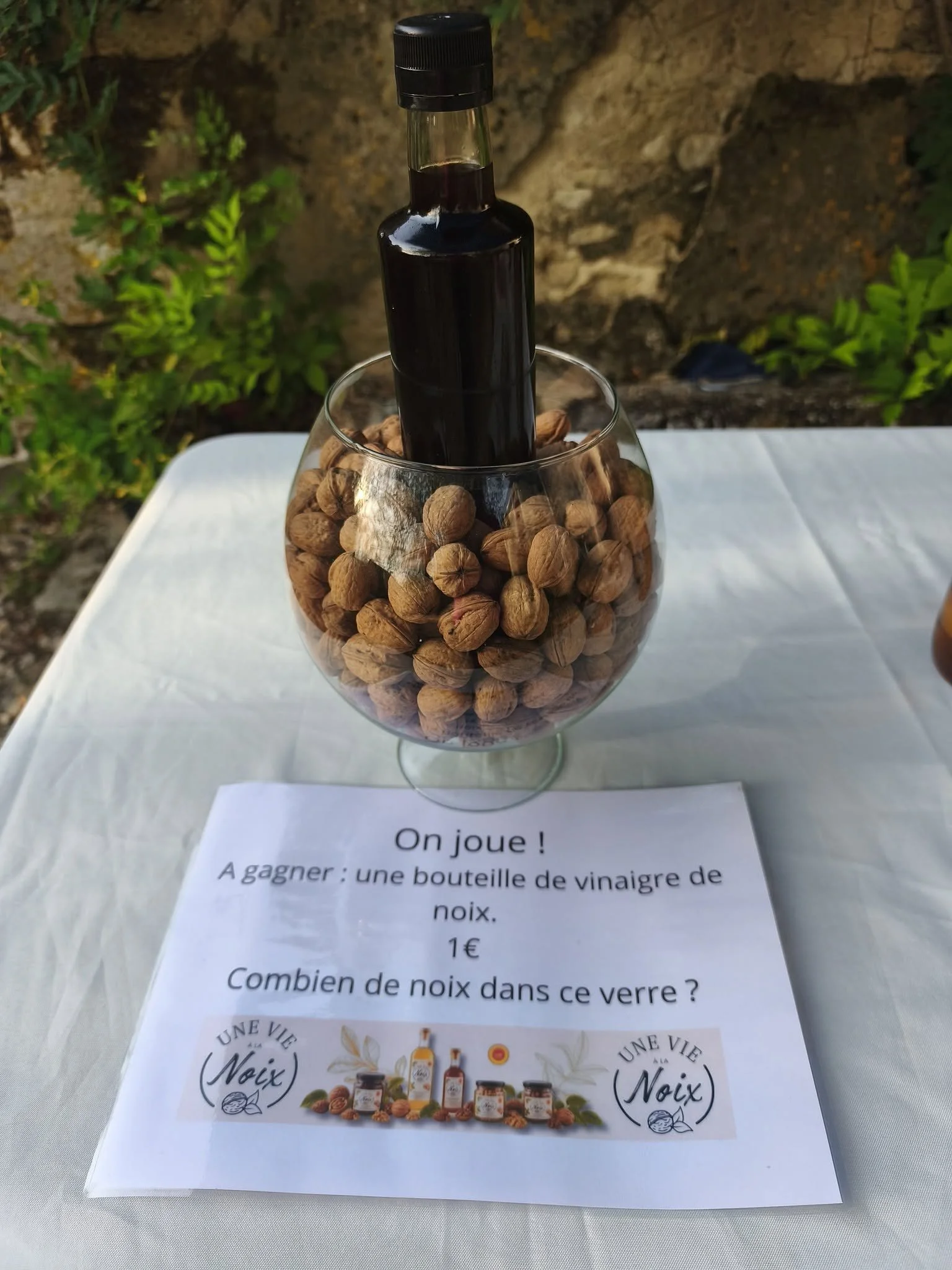 Une bouteille de vinaigre de noix dans un verre rempli de noix, placé sur une table avec un texte en français à côté.