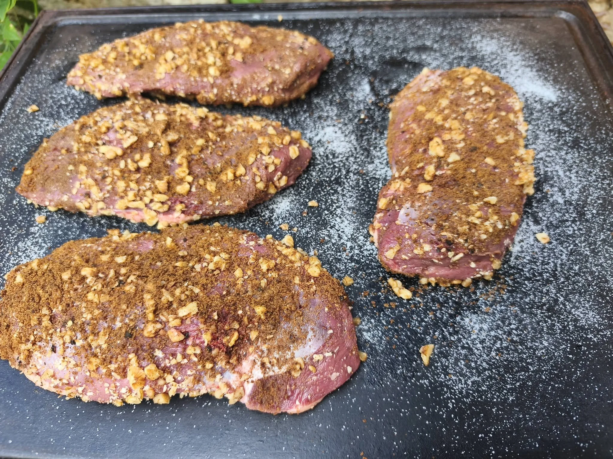 Steaks de viande en train d'être assaisonnés avec des épices et des noix hachées.