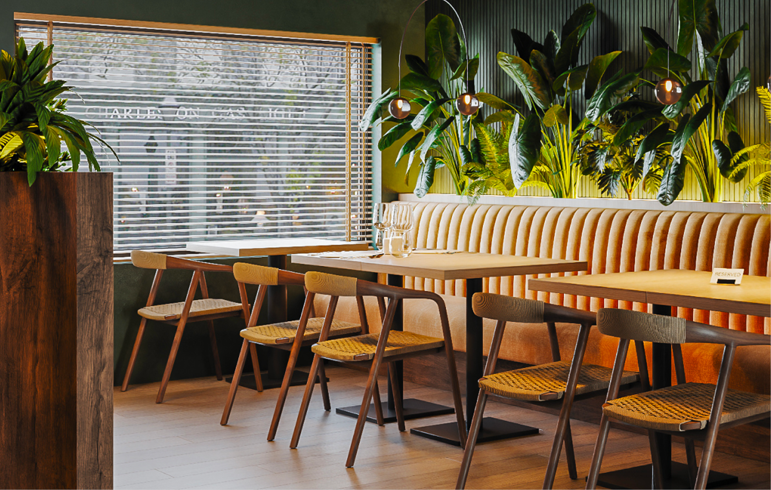 Lichte eetruimte in Bistro Verde met houten tafels, een gestoffeerde bank, grote groene planten en een raam met lamellen