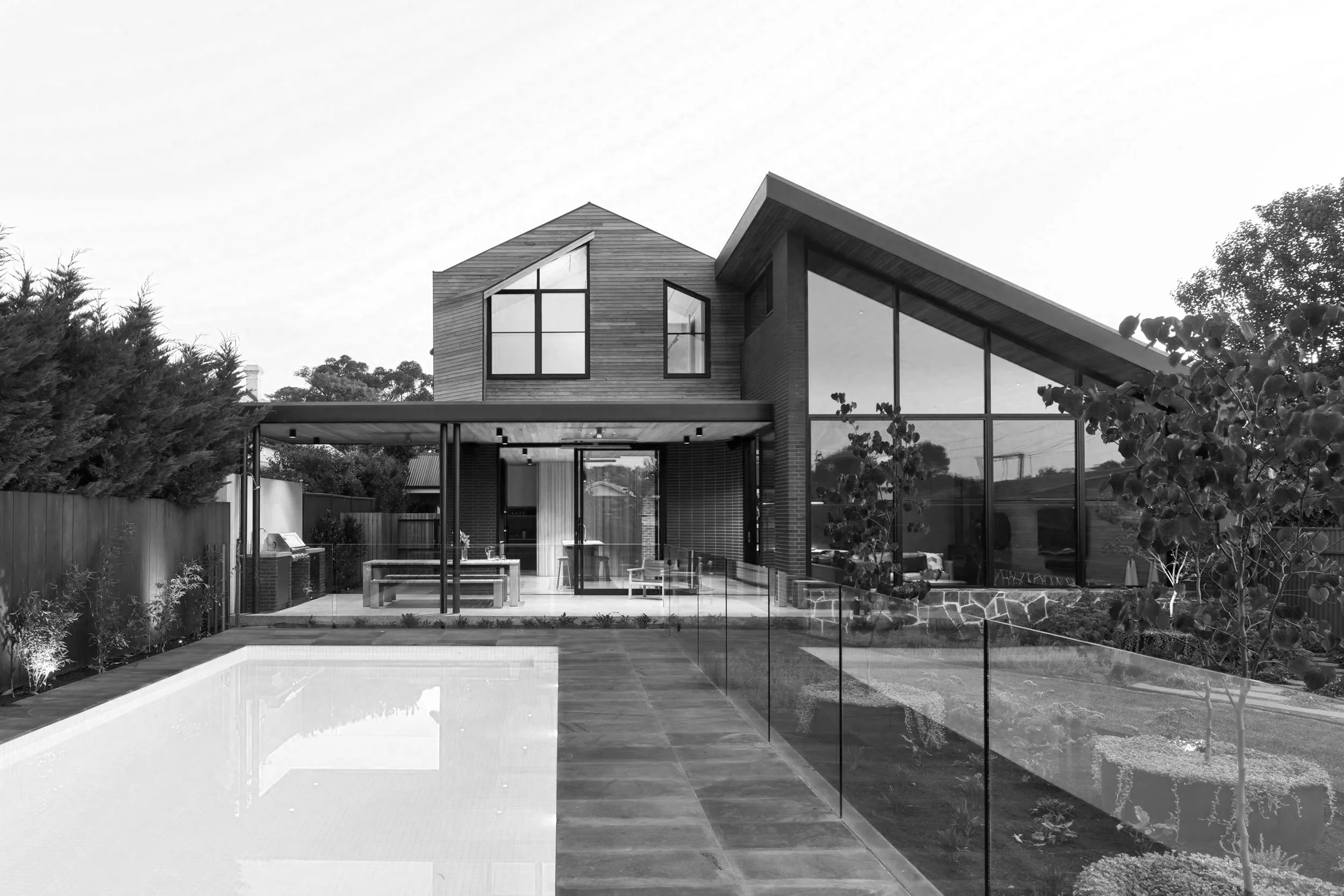 Modern two-story home with angular rooflines, expansive glass walls, landscaped yard, outdoor kitchen, and swimming pool
