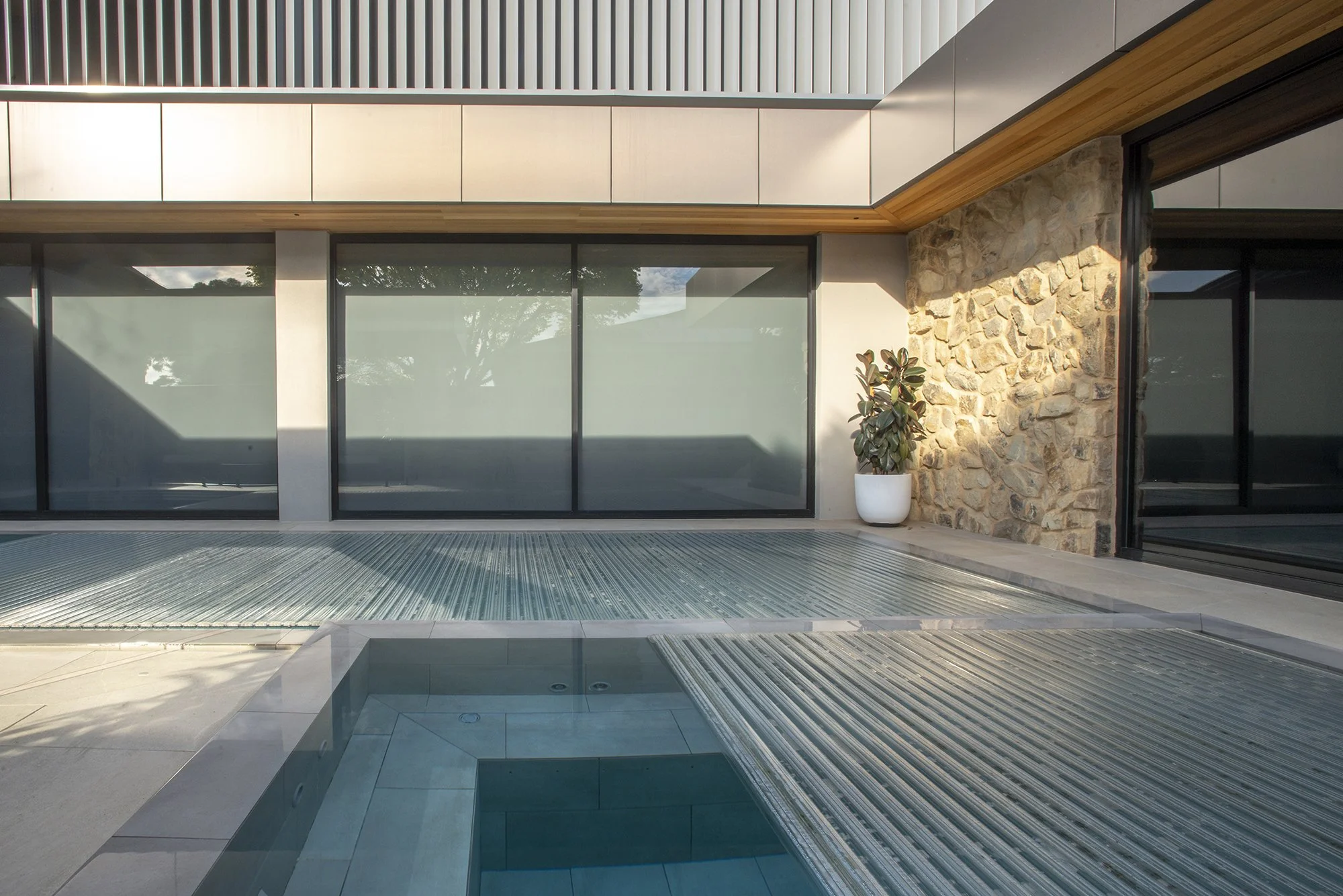 Modern indoor pool with glass walls, stone accent wall, wood ceiling, and potted plant