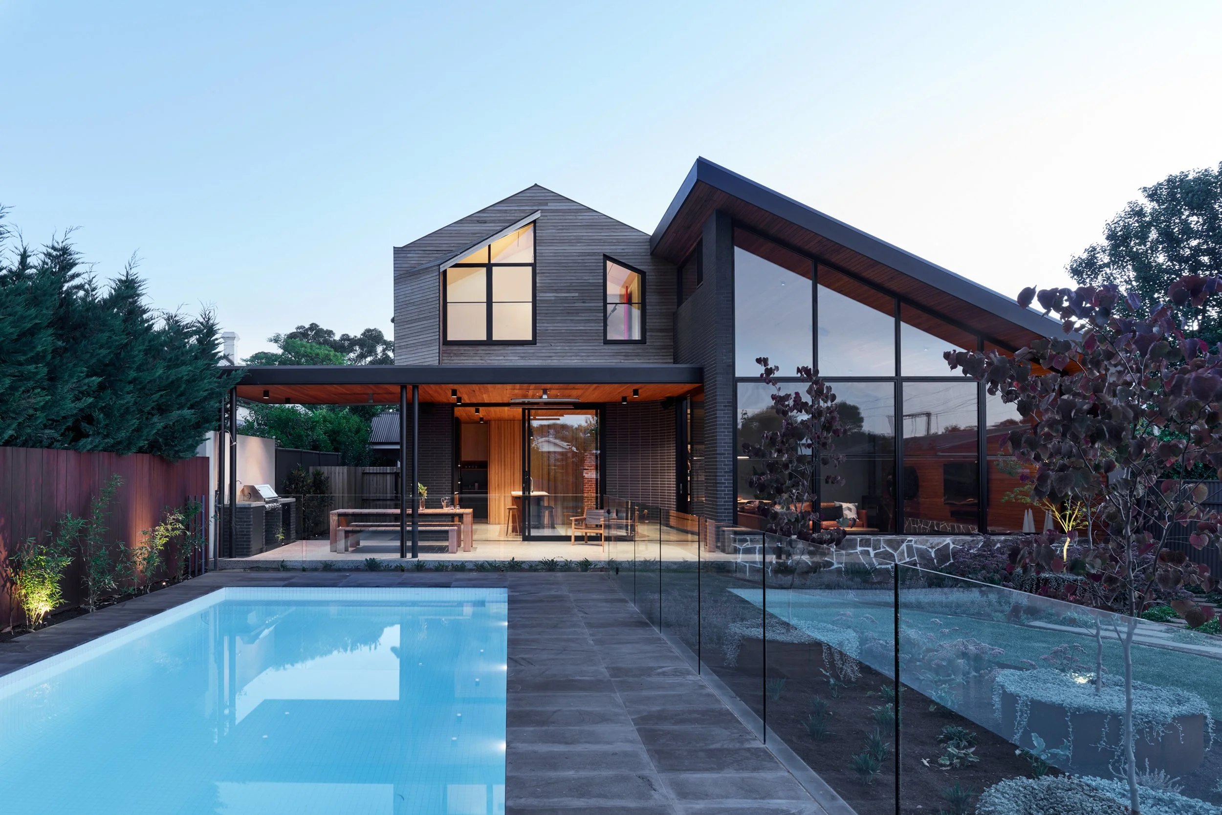 Modern two-story home with floor-to-ceiling windows, covered patio, landscaped yard, and outdoor swimming pool