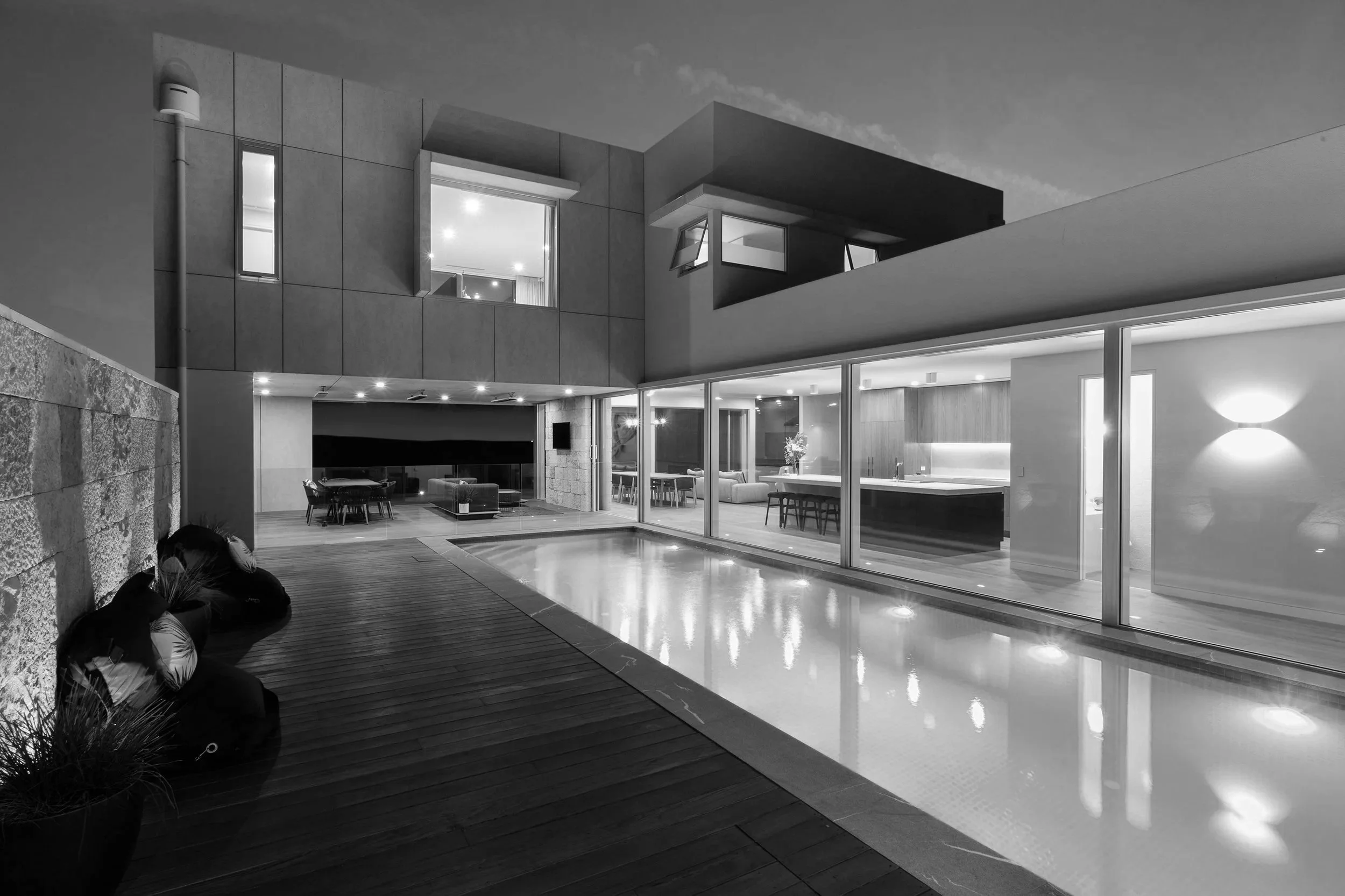 Modern luxury home with an indoor pool, wood deck, glass walls, and open-plan living spaces at night