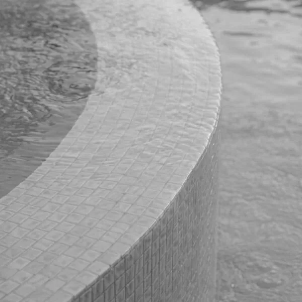 Curved tiled edge of a swimming pool beside rippling water