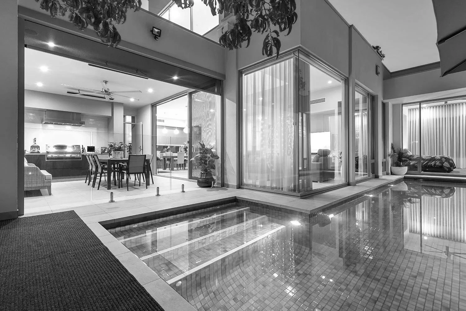 Modern open-plan home interior with kitchen, dining area, floor-to-ceiling windows, and indoor swimming pool