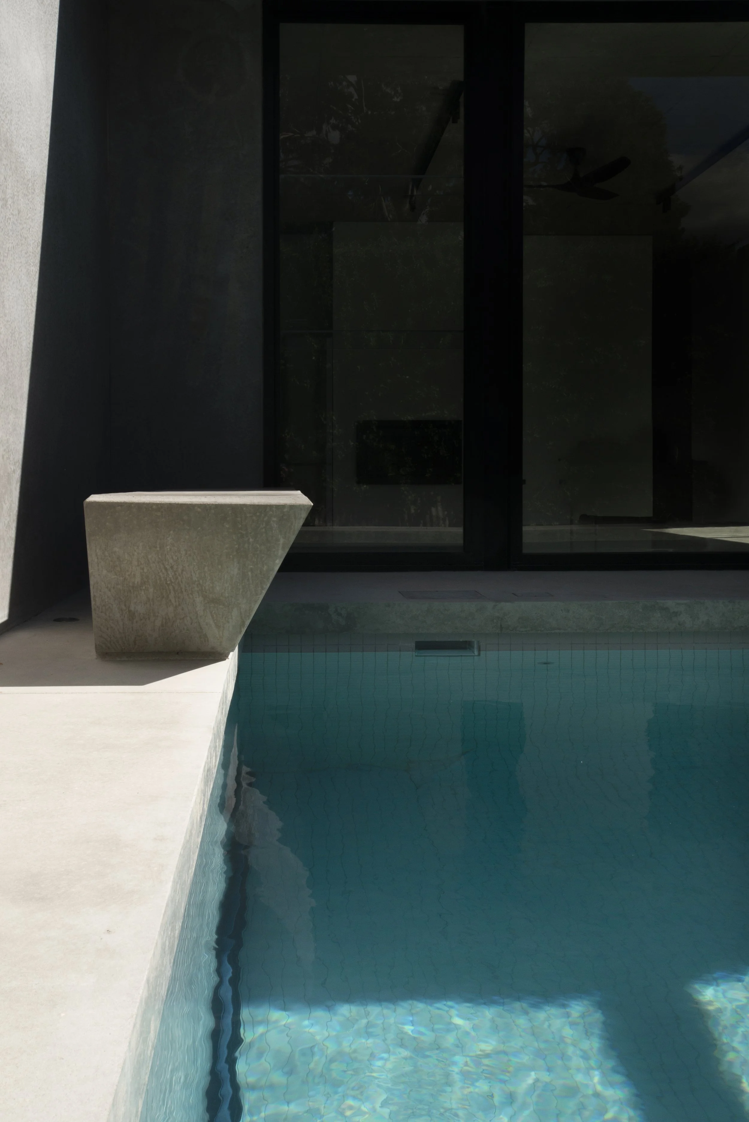 Modern swimming pool with turquoise water, concrete planter, and dark reflective windows