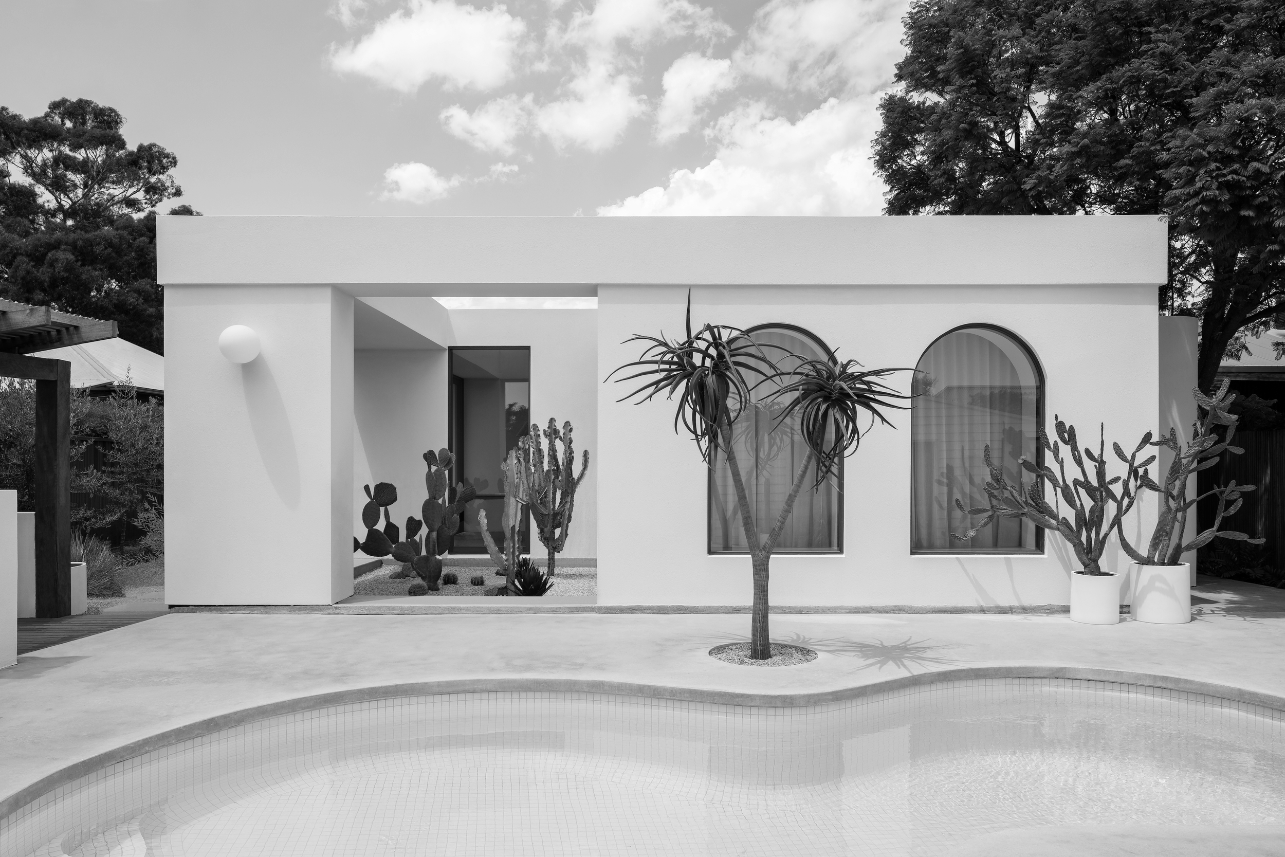 Modern white house with arched windows, cactus landscaping, and a curved swimming pool