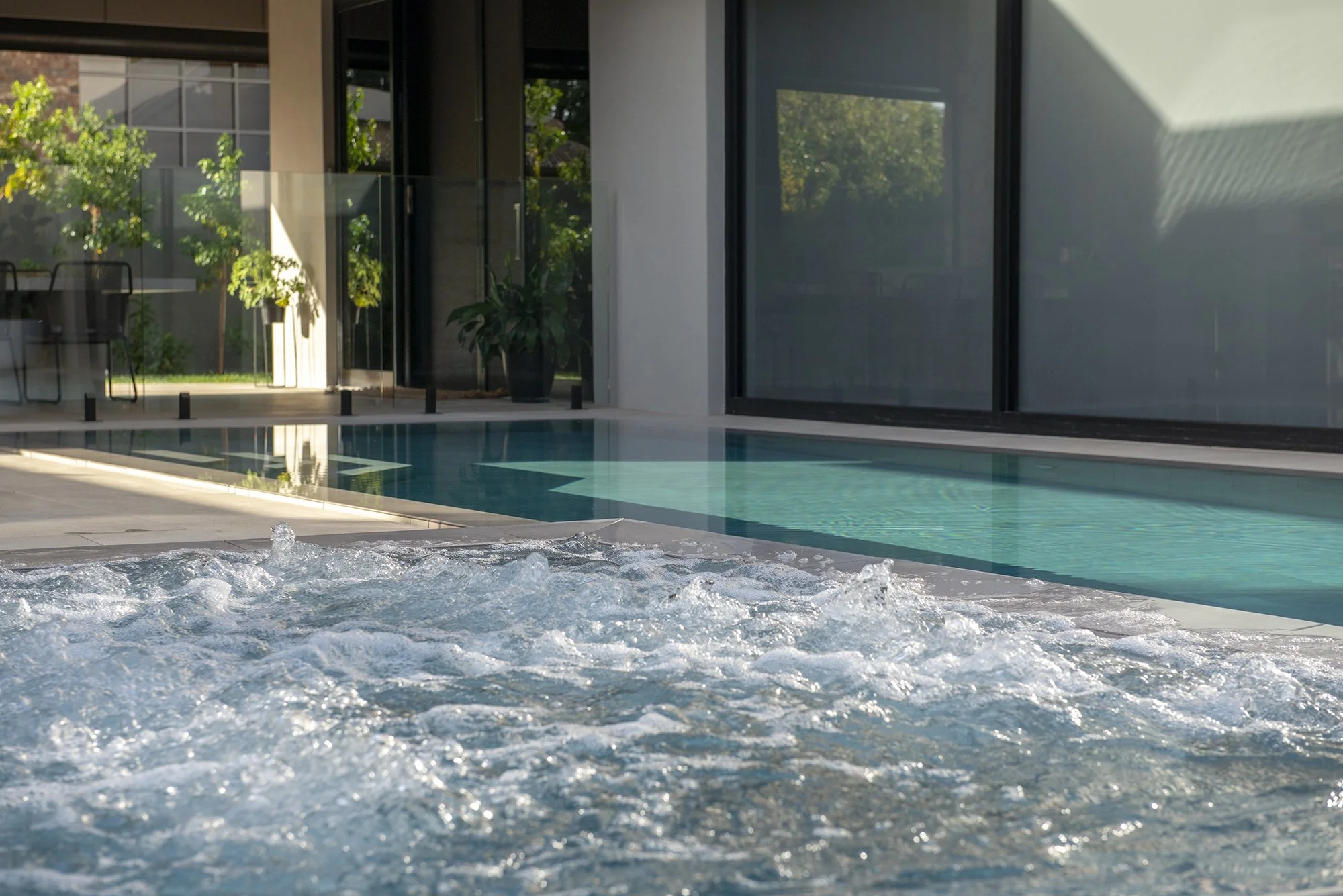 Indoor swimming pool and bubbling spa with floor-to-ceiling windows and modern patio seating