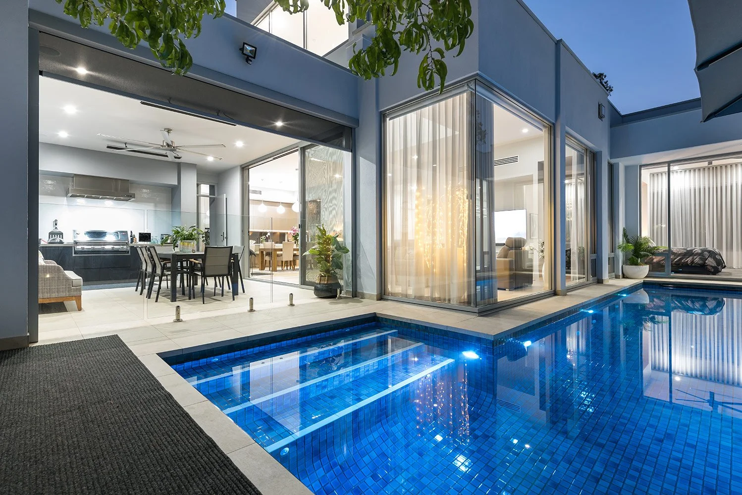 Modern home with a blue-tiled indoor pool, open-plan kitchen, dining area, and glass walls