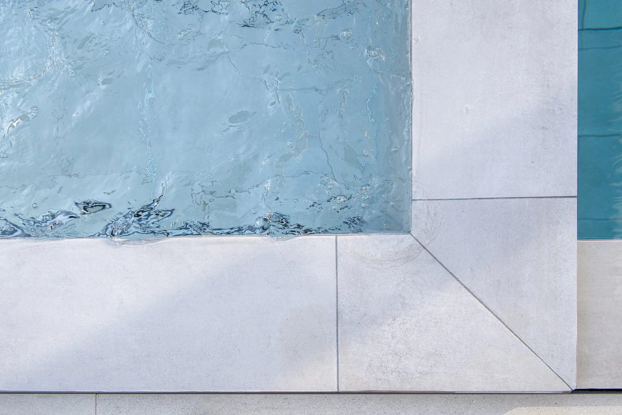 Close-up of rippling blue swimming pool water beside light gray tiled pool decking