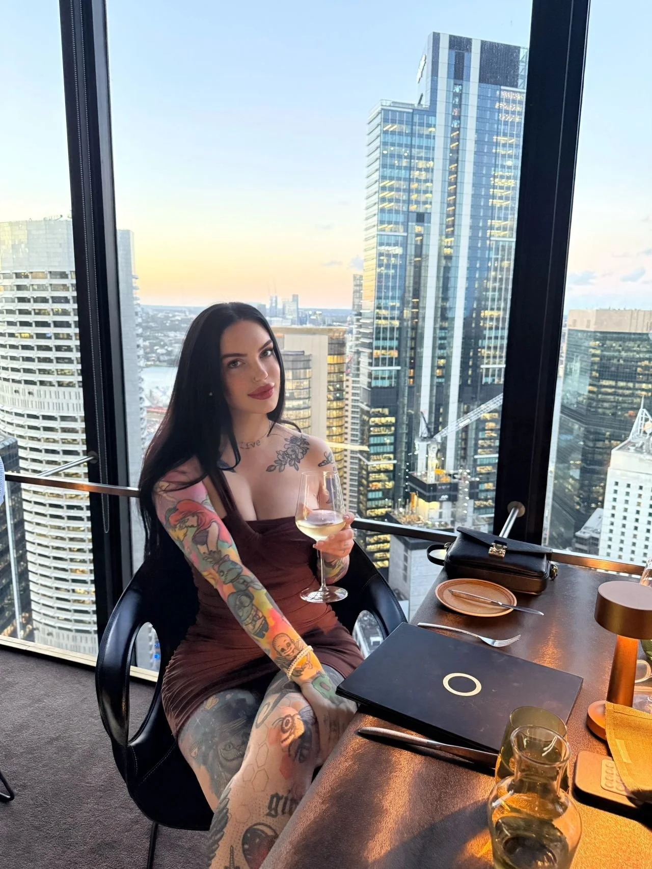 Amity Addams sharing wine against the lights of the City skyline.
