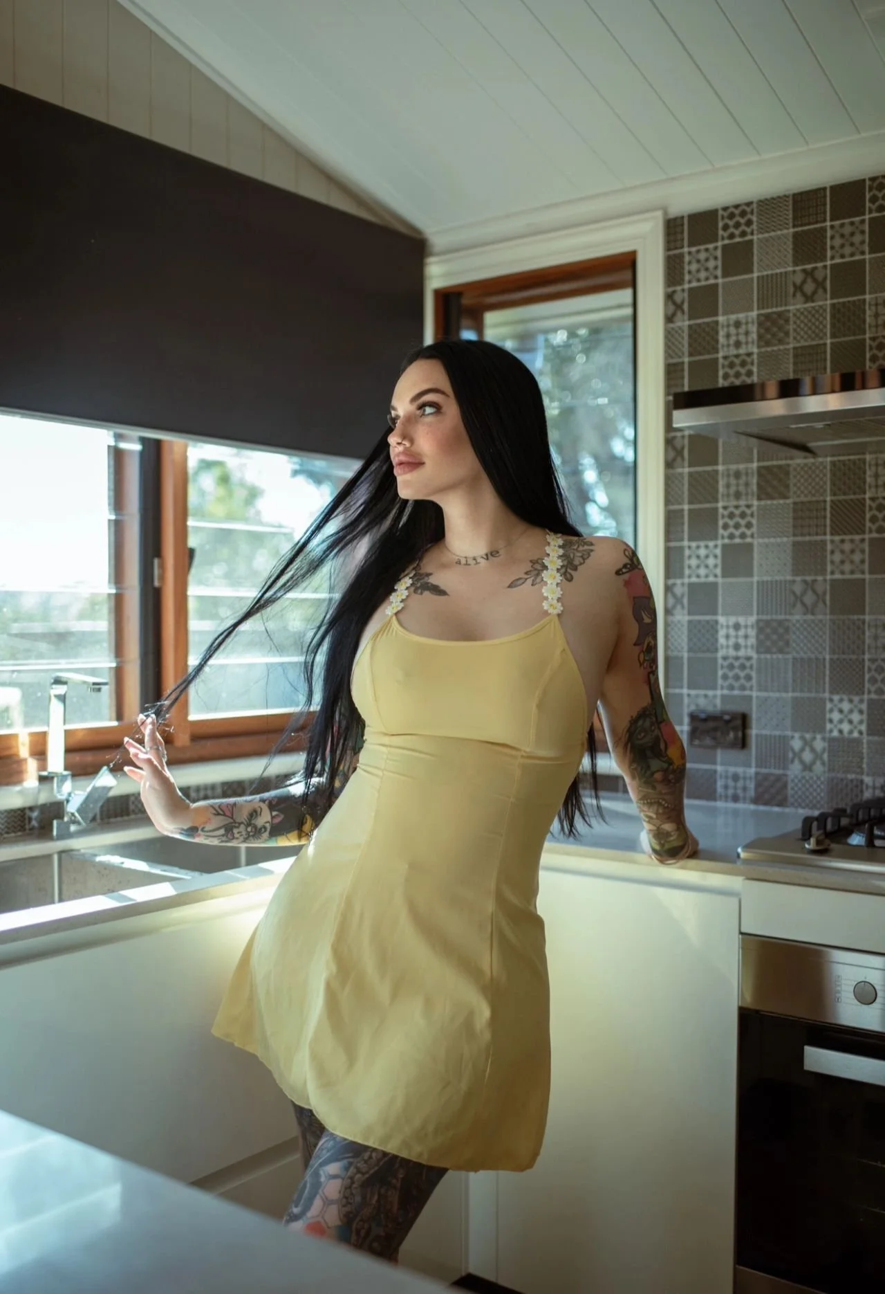 Amity Addams wearing a fitted yellow dress beside a sunlit window.
