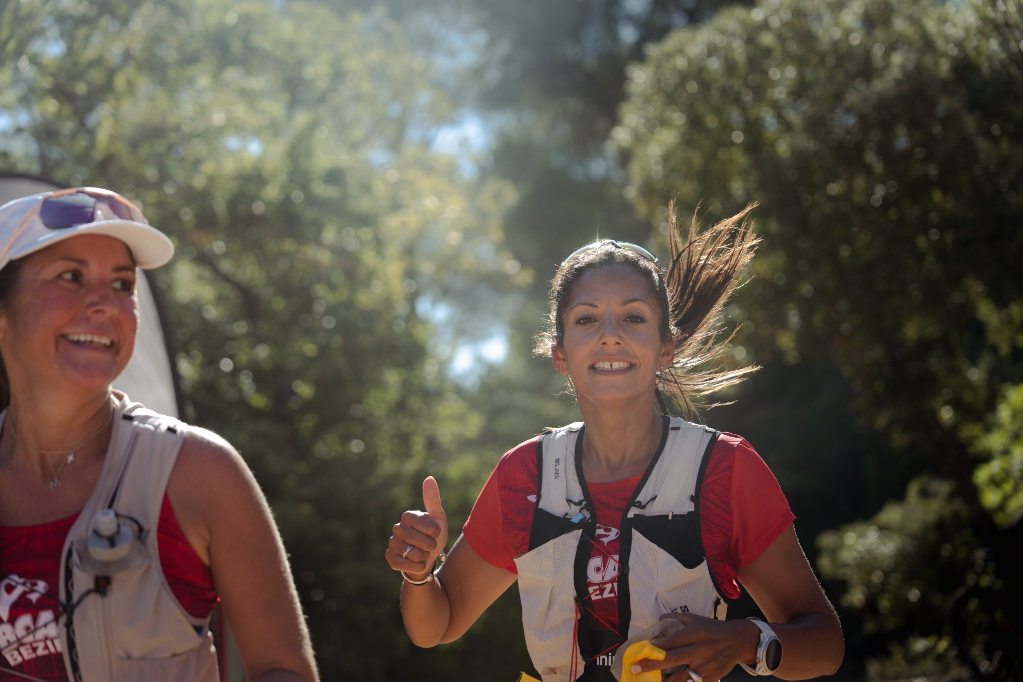 Groupe de personnes courant en forêt lors d'une course ou d'un événement sportif. Le soleil brille à travers les arbres.