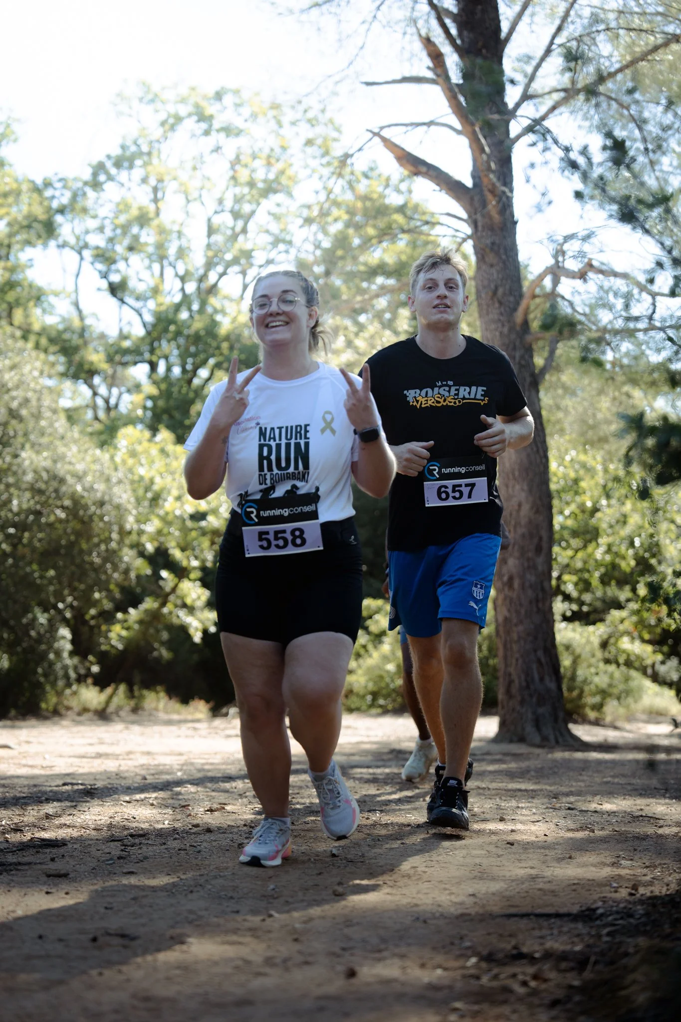 Deux coureurs participent à une course en plein air, dans un parc avec des arbres, portant des dossards numérotés 558 et 657.