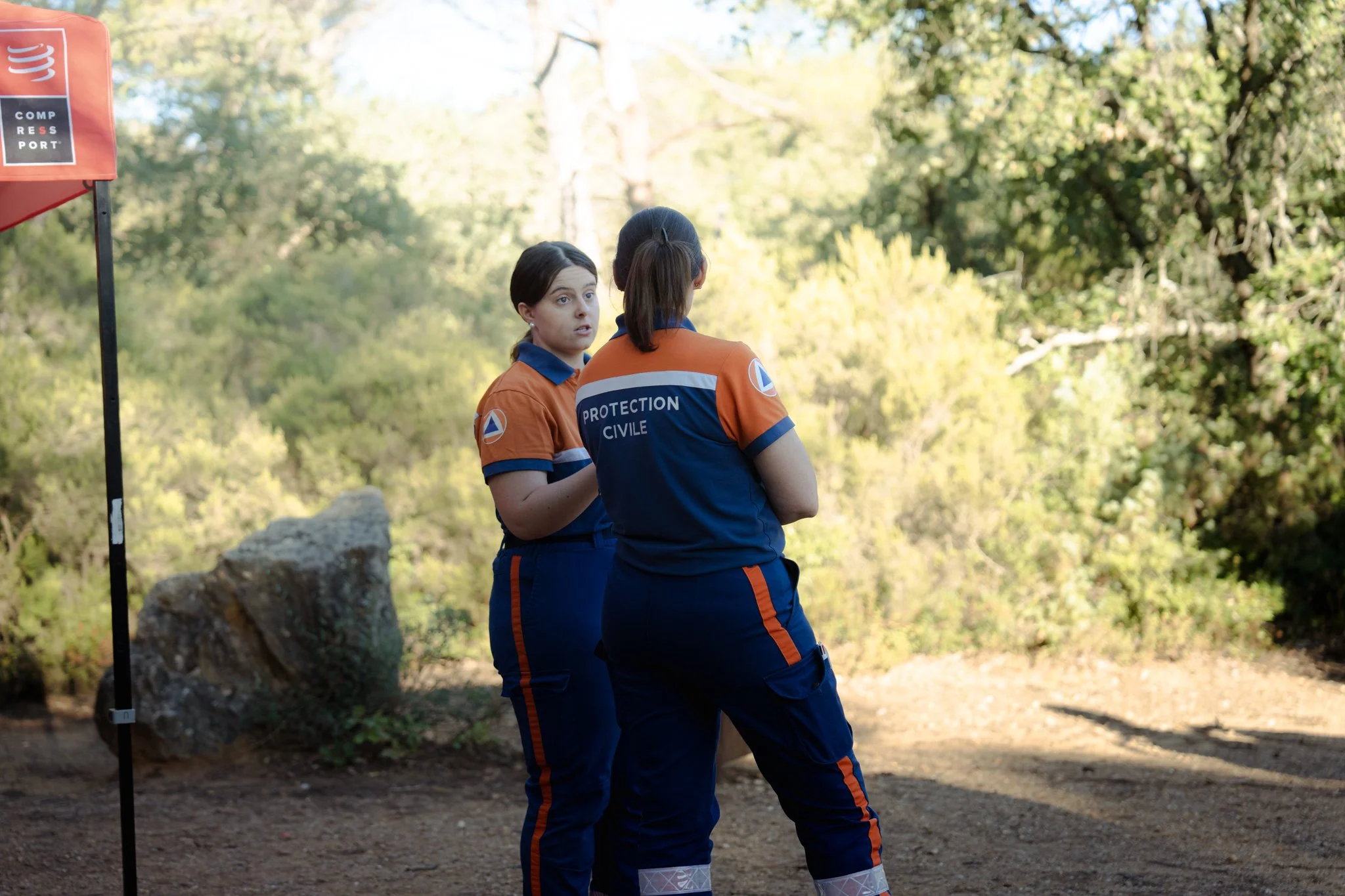 Deux femmes en uniforme de protection civile discutent dans un environnement forestier.