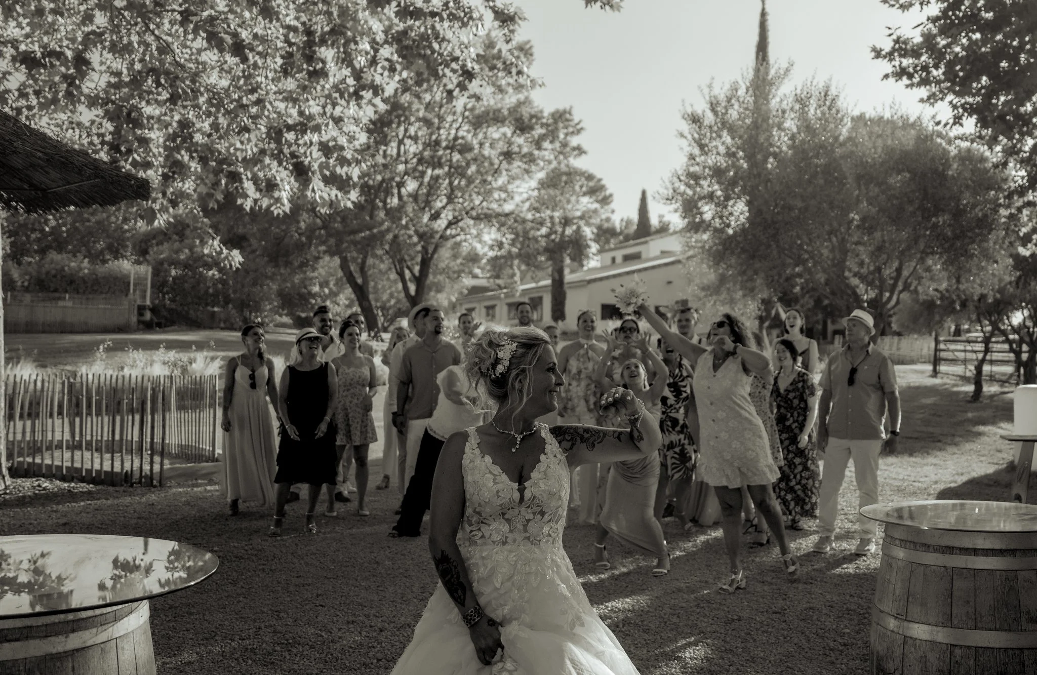 Un groupe de personnes habillées en vêtements d'été, apparemment lors d'une fête ou mariage en extérieur, avec un arbre et une maison en arrière-plan.