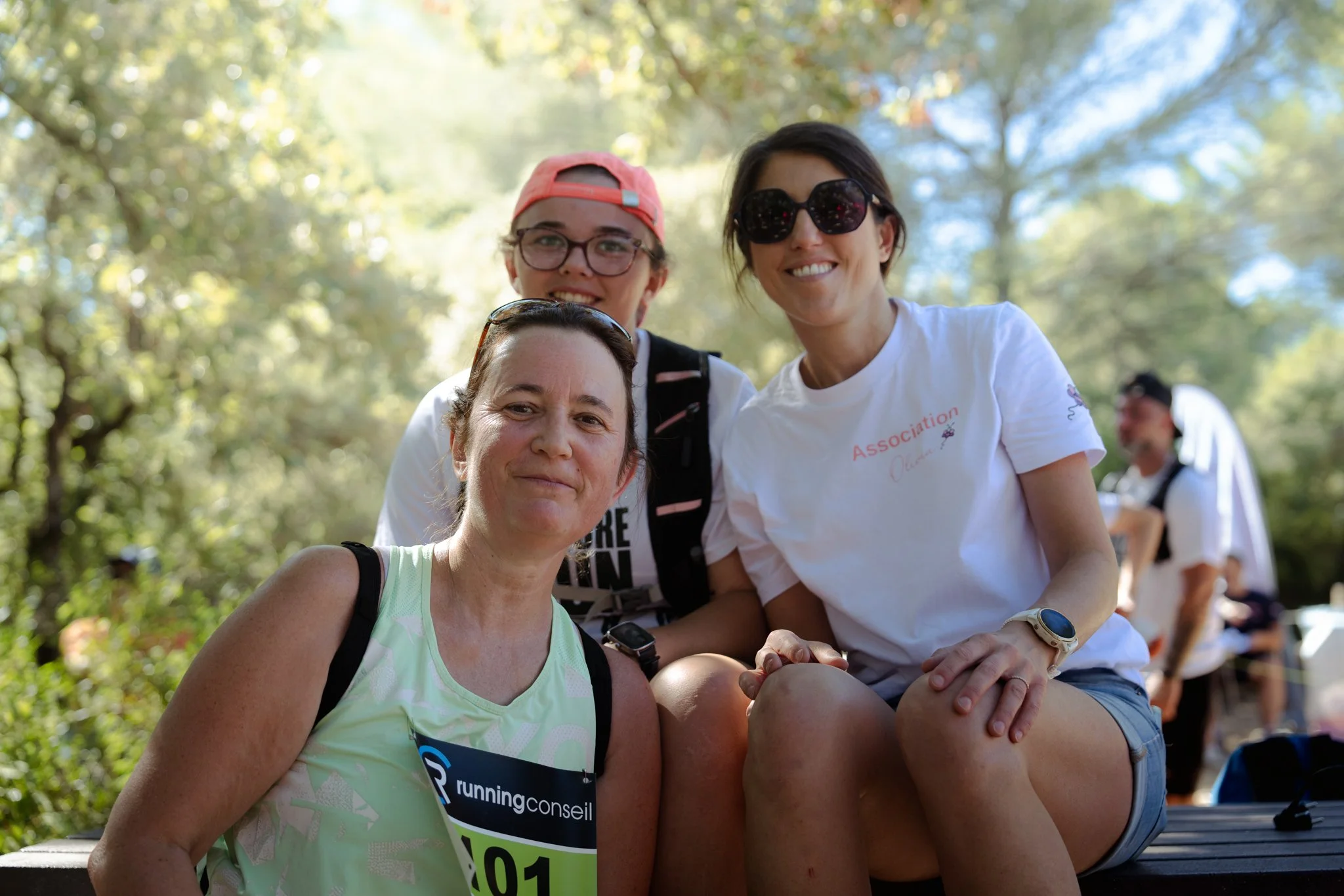 Groupe de femmes souriantes lors d'un événement en plein air sous un arbre, portant des vêtements de sport et des badges de course.
