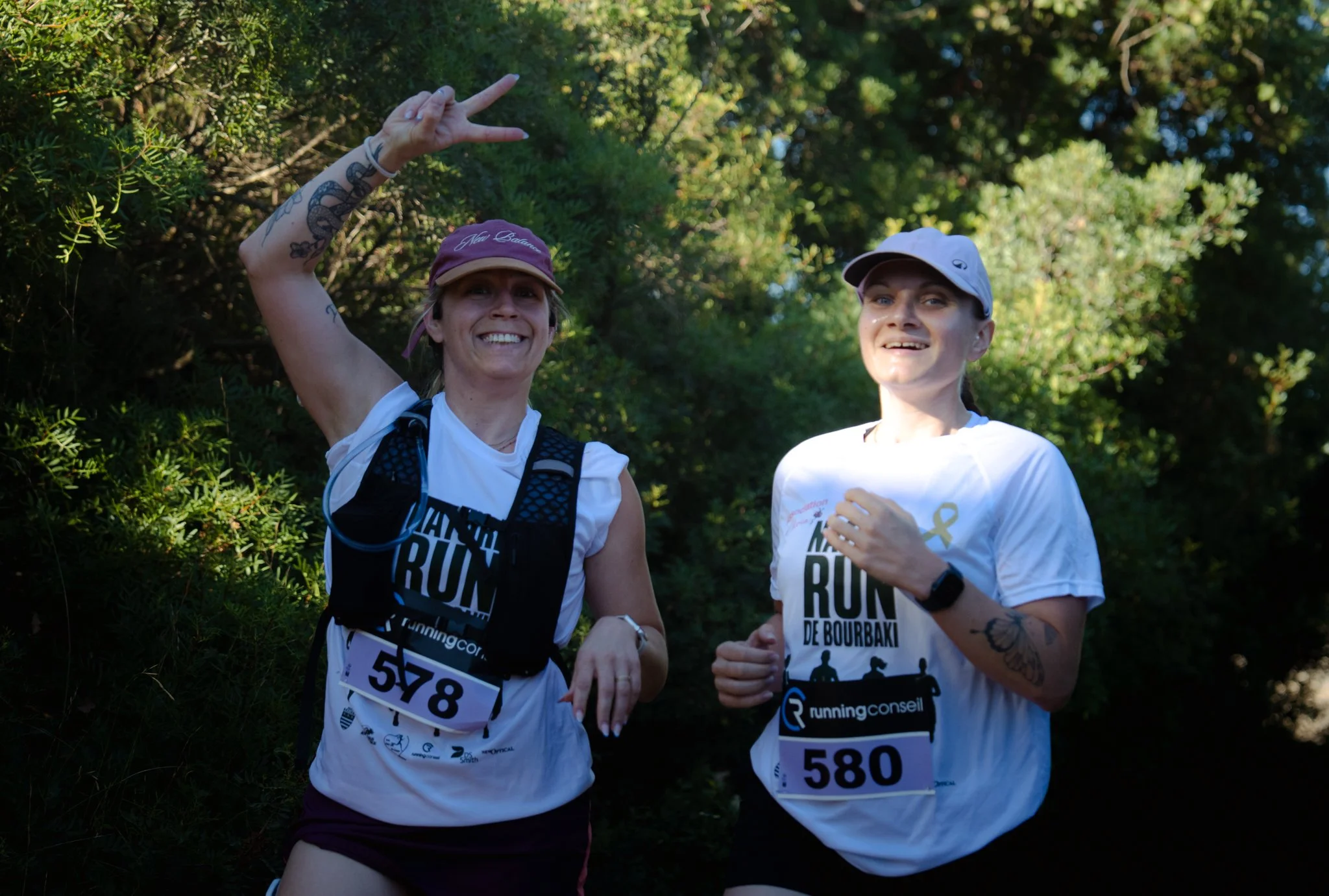 Deux femmes courent lors d'une course en plein air, portant des tenues de course et des bips avec les numéros 578 et 580, entourées de végétation verte.