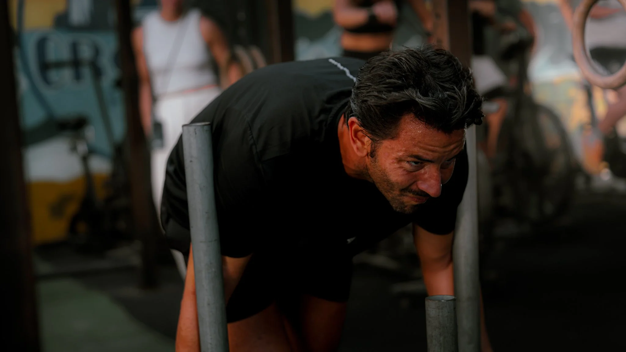 Un homme s'entraîne dans une salle de sport, plié en avant avec des barres de musculation autour, montrant un effort physique intense.
