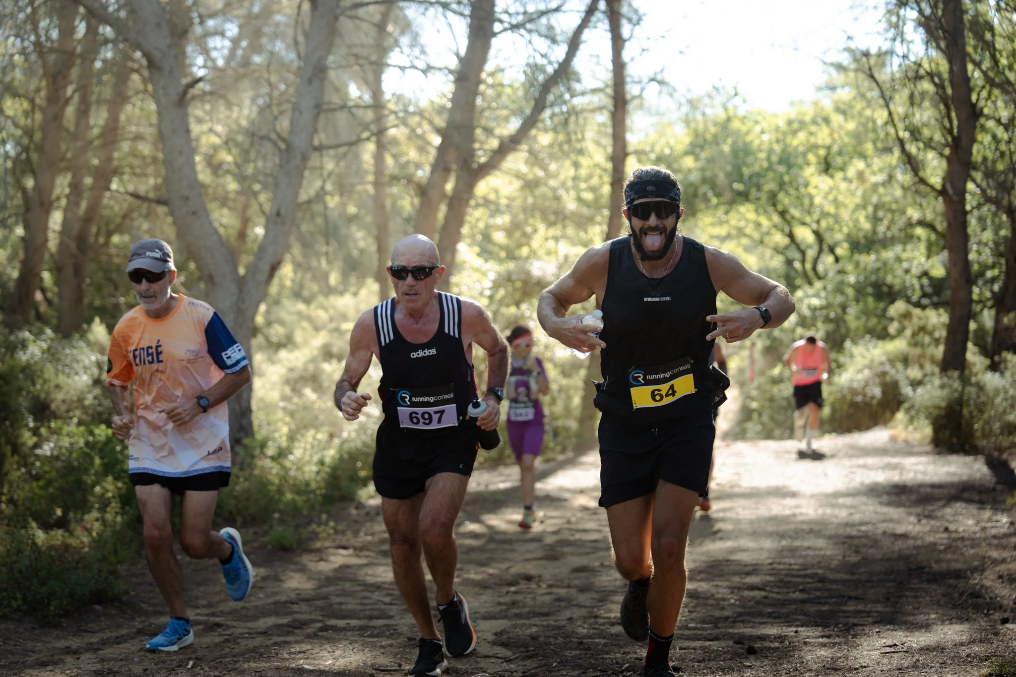 Groupe de coureurs participant à une course en forêt, portant des numéros et des équipements de sport.