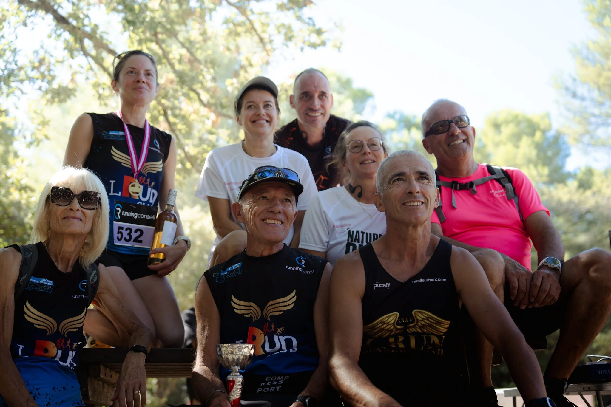 Groupe de personnes souriantes lors d'un événement en plein air, portant des vêtements de sport avec des médailles et trophée.
