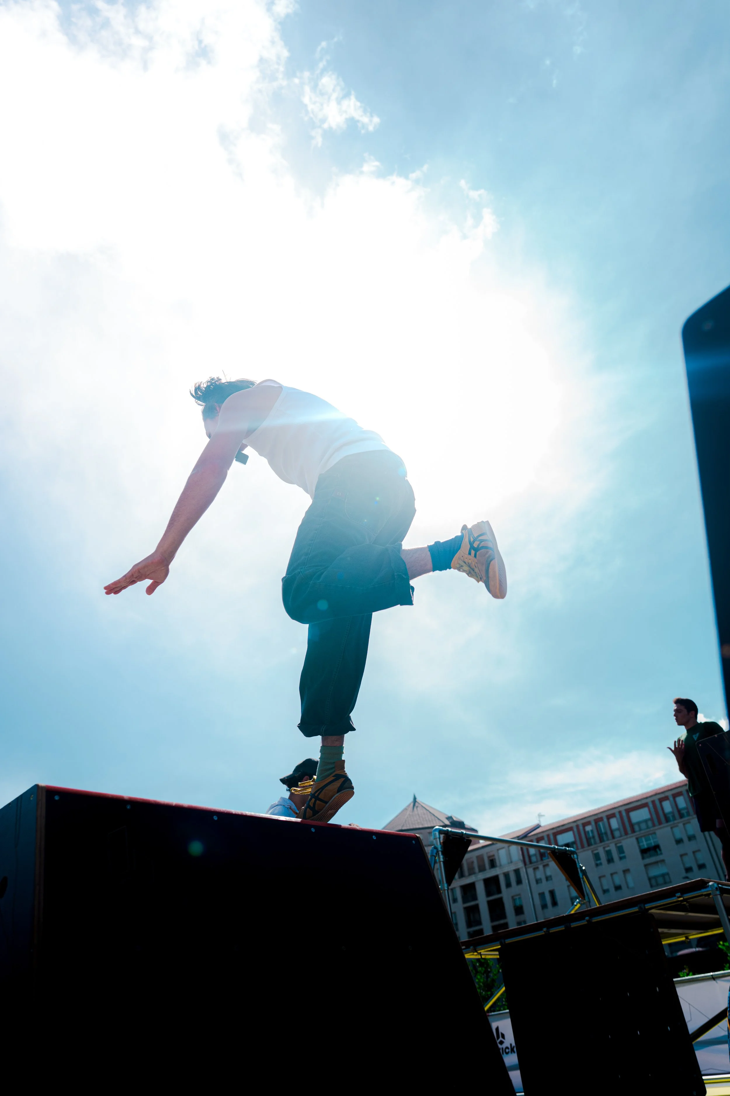 Un jeune homme en équilibre sur une plateforme lors d'une performance de jonglerie en extérieur sous un ciel ensoleillé.